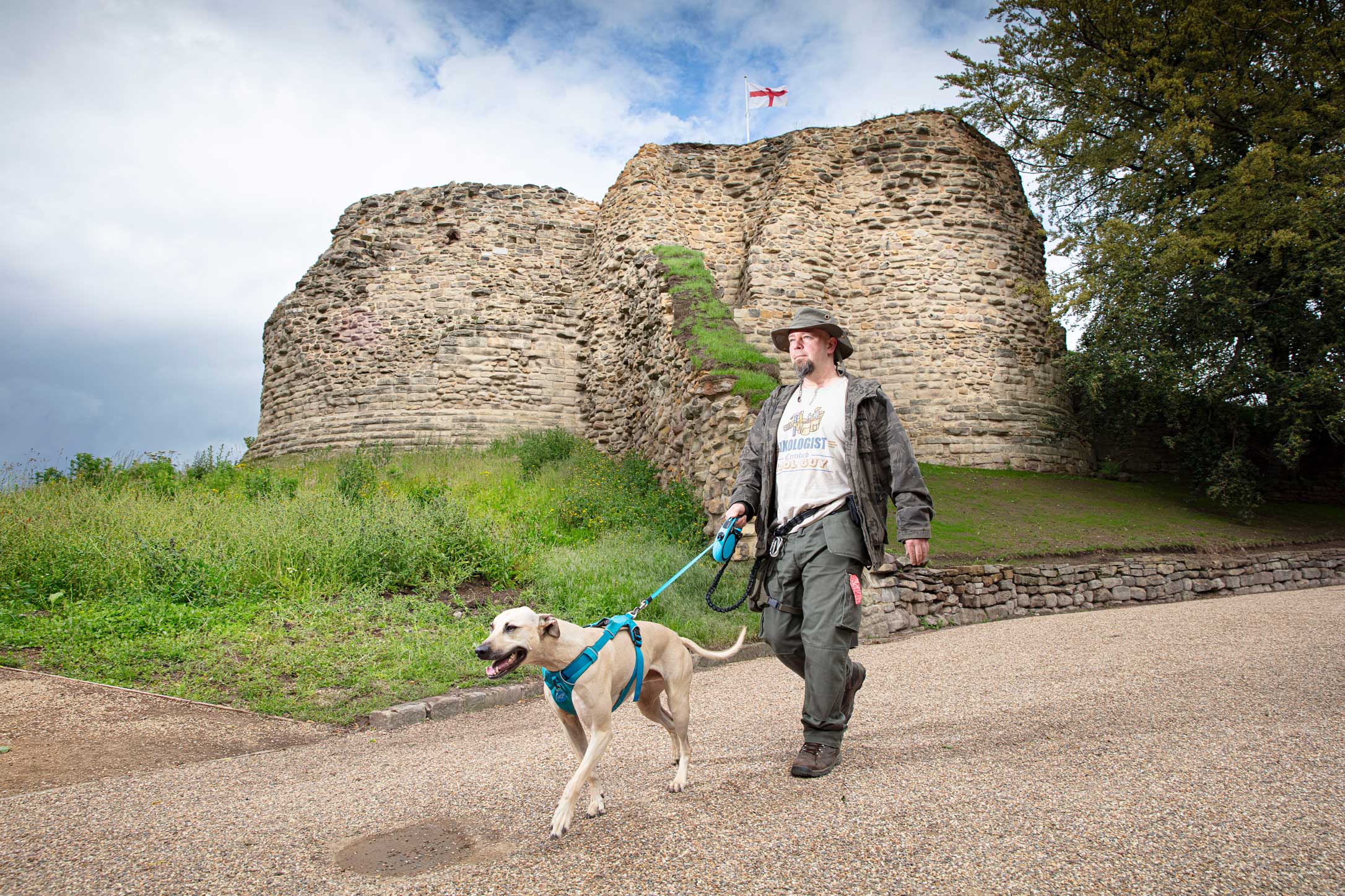 A man walking a dog with the ruins of a castle in background.