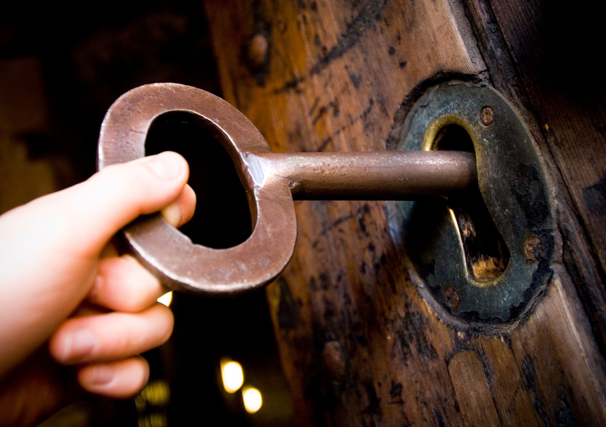 A child's hand on a large old fashioned key in a castle door.