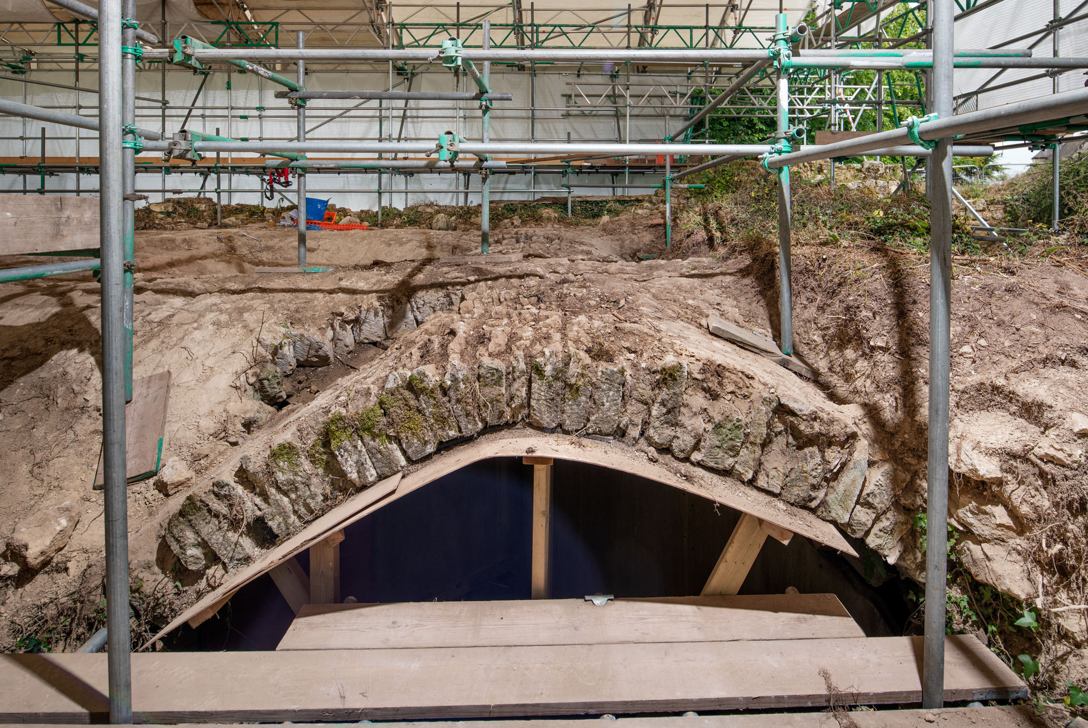A stone vaulted undercroft under excavation, protected by plastic sheeting spanned on scaffolding.