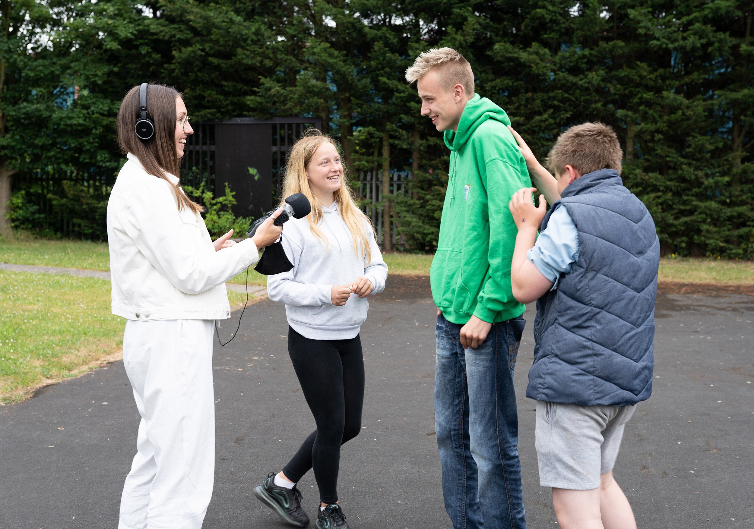 A woman holding a microphone and wearing headphones interviewing three other people