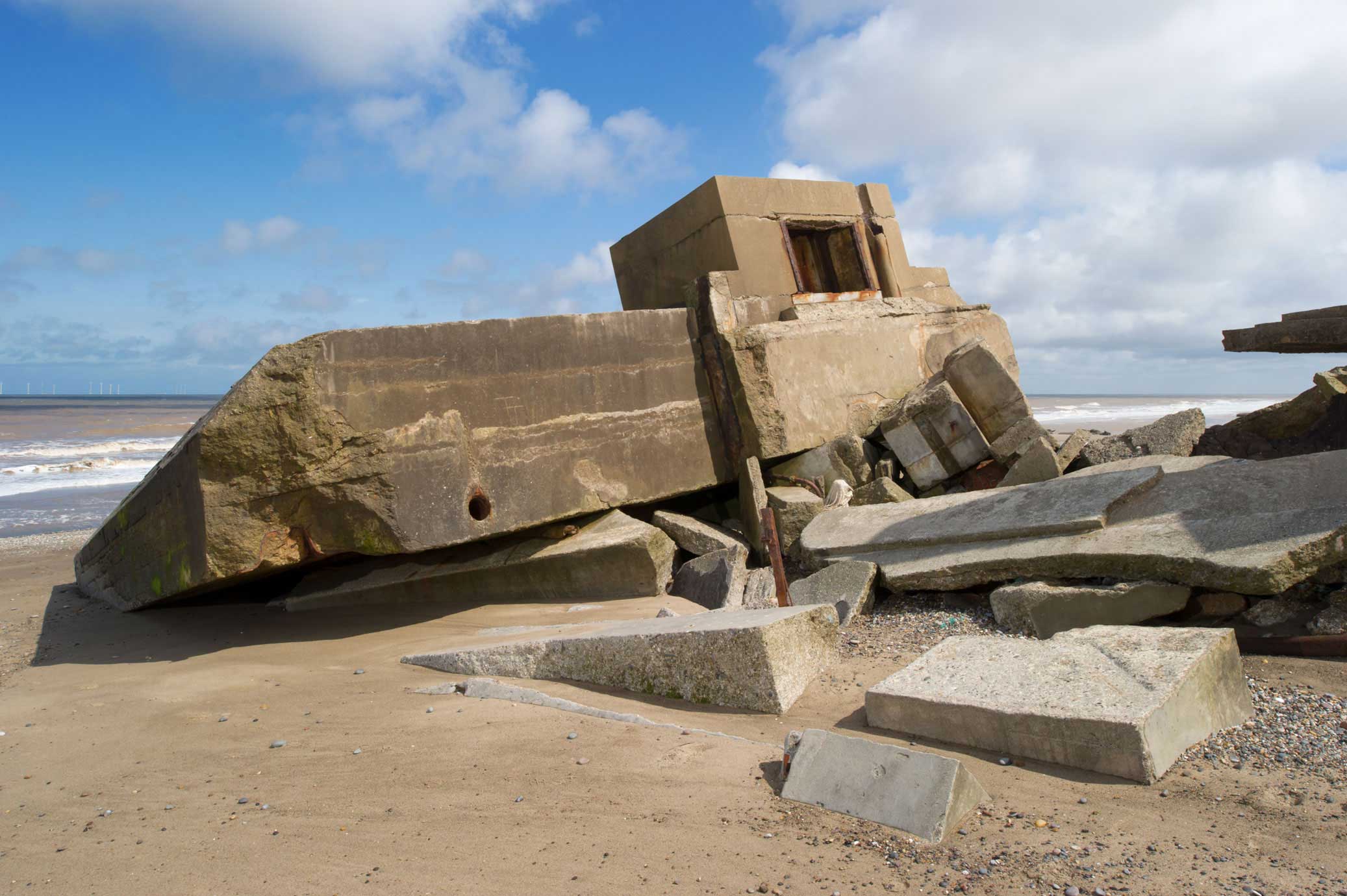 The remains of a concrete defensive emplacement that has collapsed onto a beach.