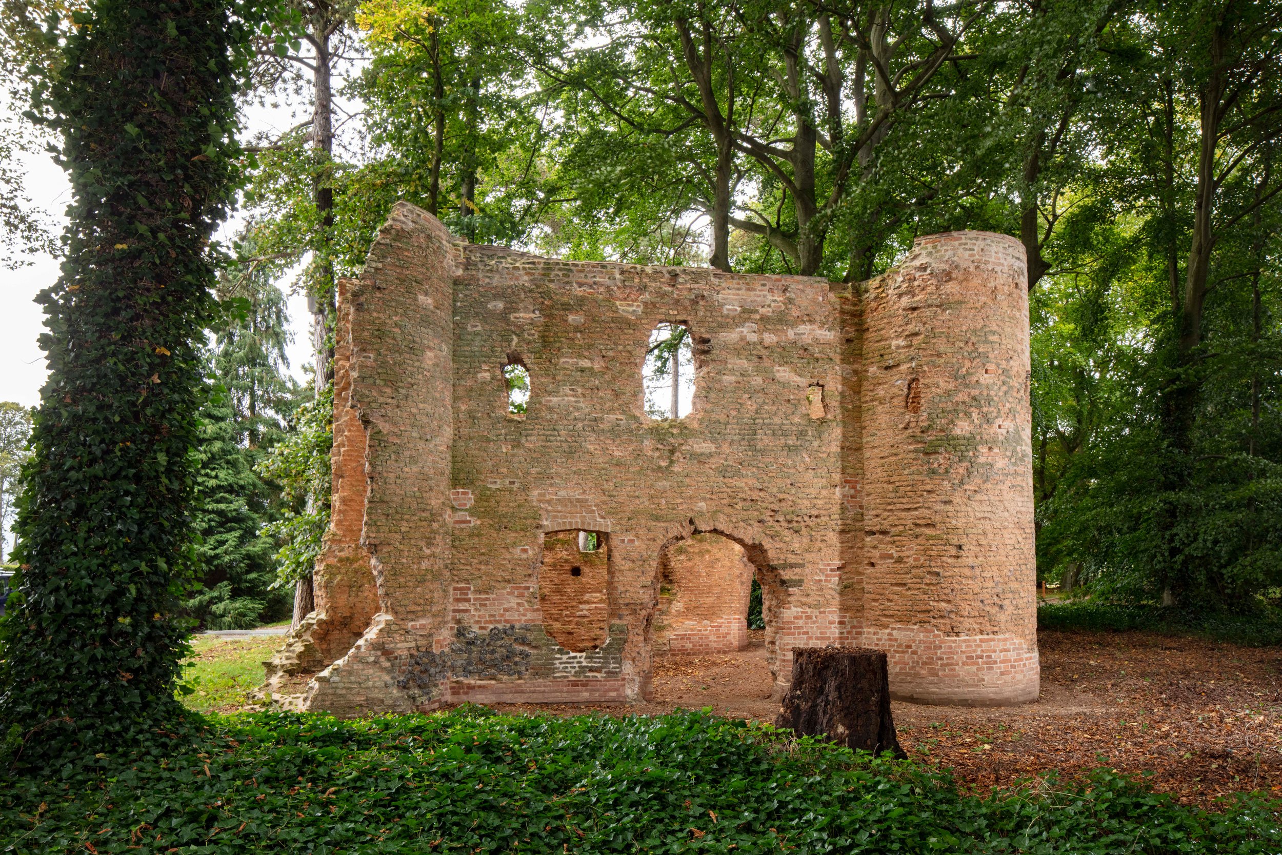 A two-storey brick ruin surrounded by trees that soar above it.