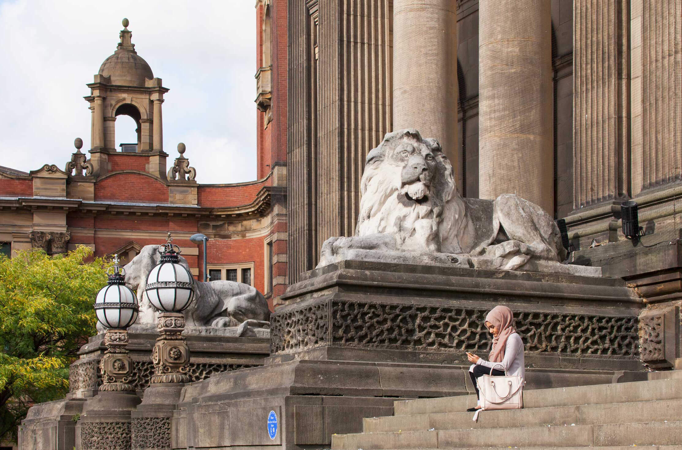 A young woman with a headscarf seated on the steps of Leeds Town Hall