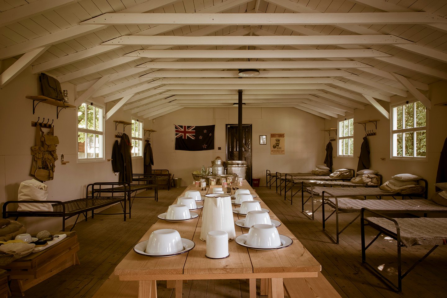 Colour photograph showing interior of wooden hut with trestle tables in centre and beds around sides