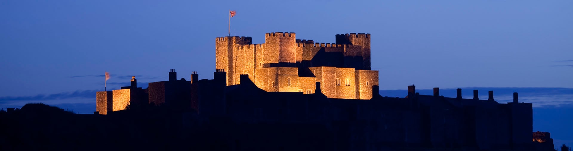 A large medieval castle keep dramatically floodlit at twilight.