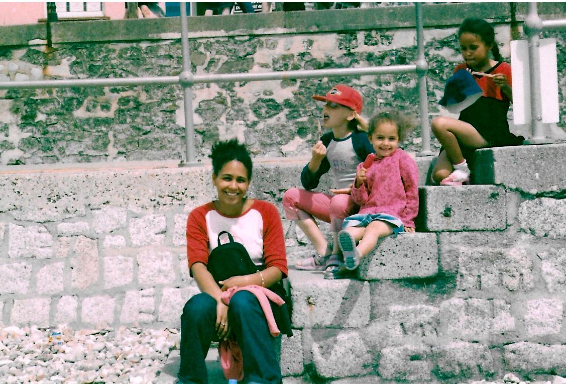 A woman and three little girls sitting on steps on the seafront at Lyme Regis.