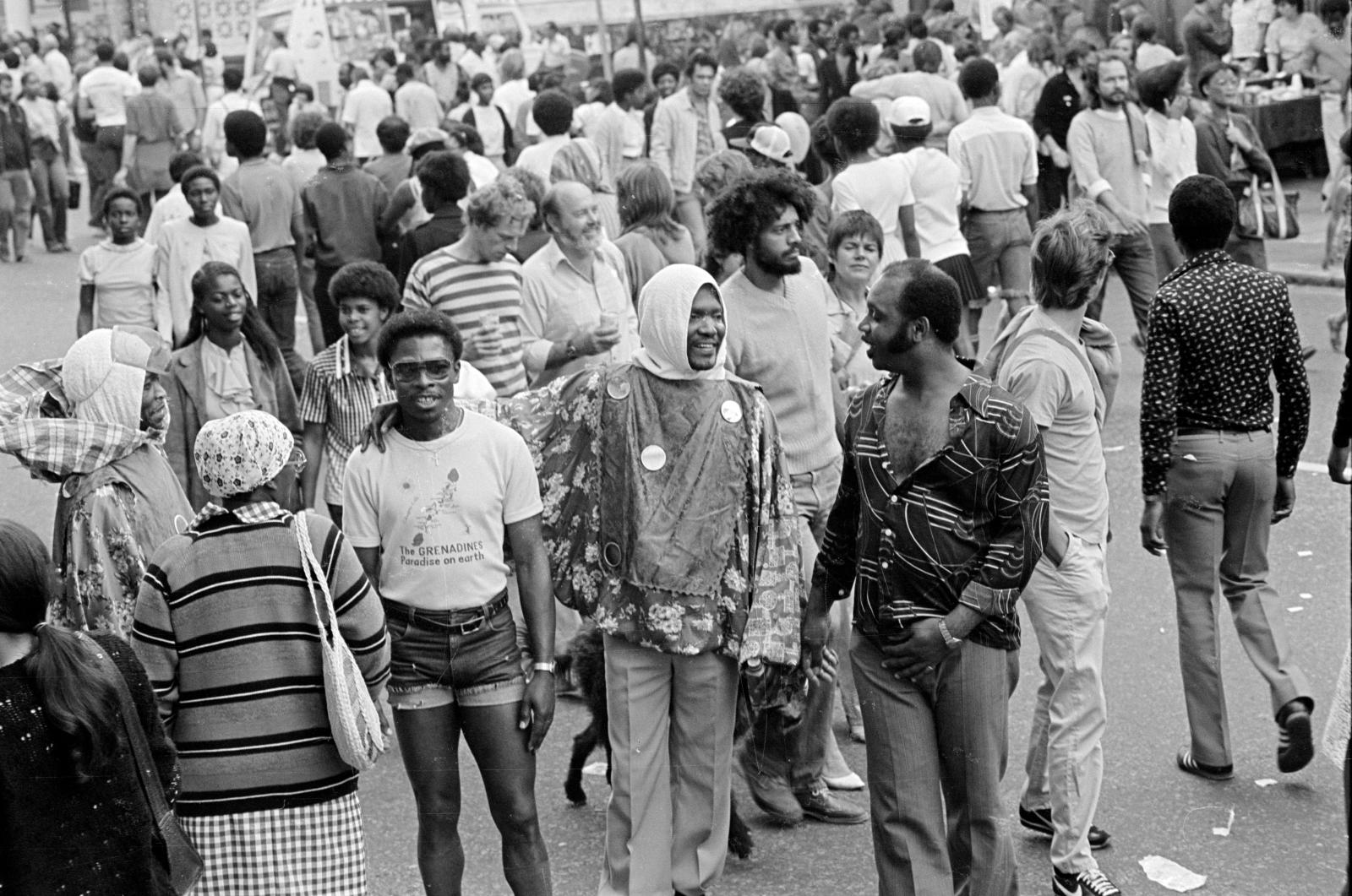 Black and white photo by John Gay of Notting Hill Carnival goers walking along a street.