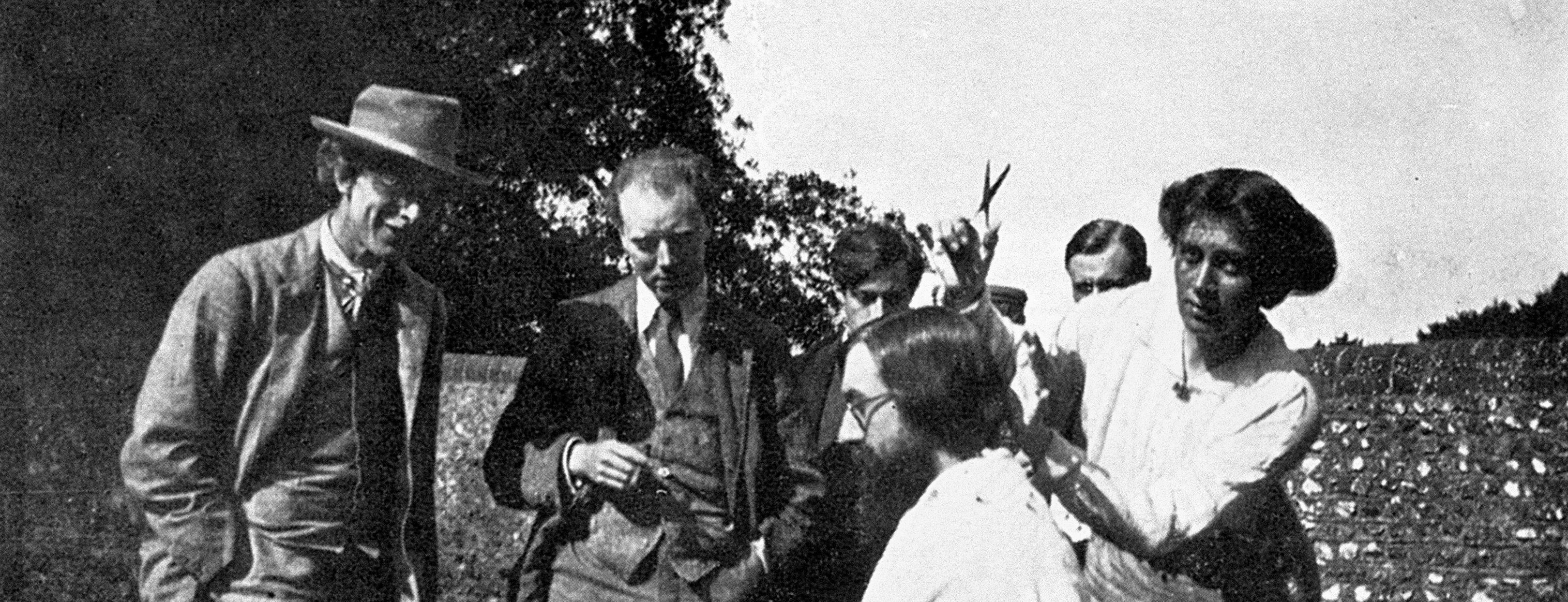 Vanessa Bell is cutting Lytton Strachey's hair while Roger Fry, Clive Bell, Duncan Grant and an unidentified guest look on