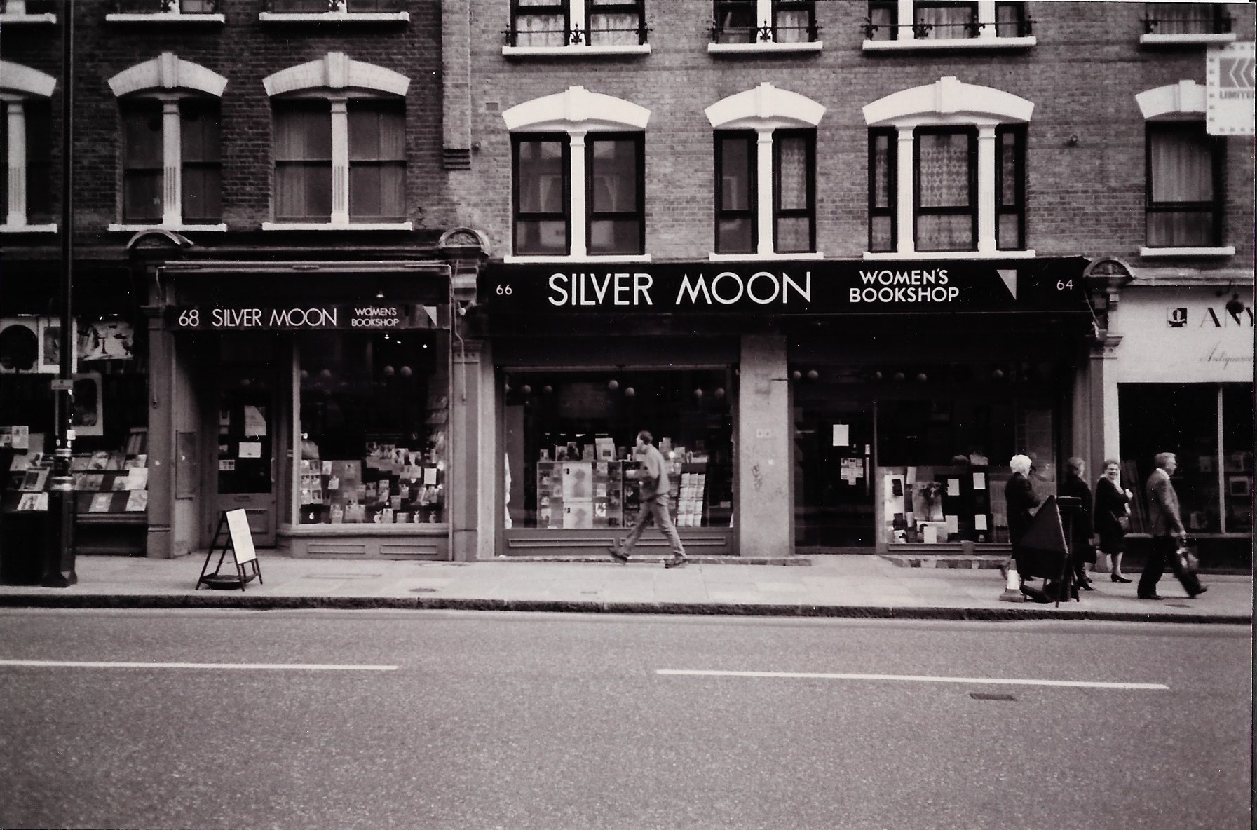 Black and white photo of the front of the Silver Moon Bookshop photographed from the street with pedestrians walking past.
