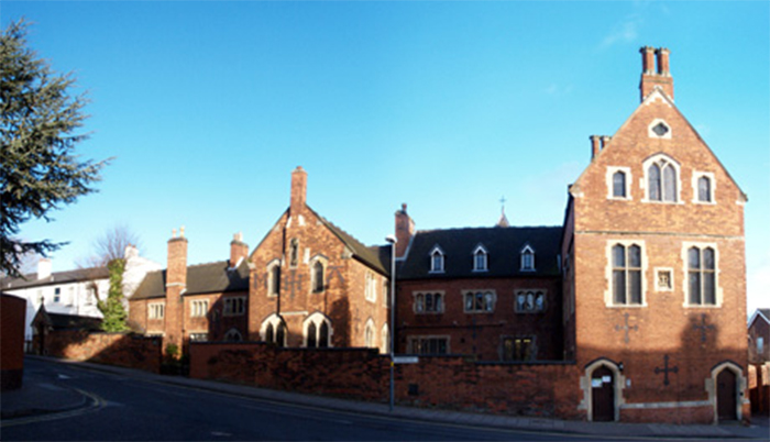 A large red brick building with multiple chimneys on a sloping residential street.