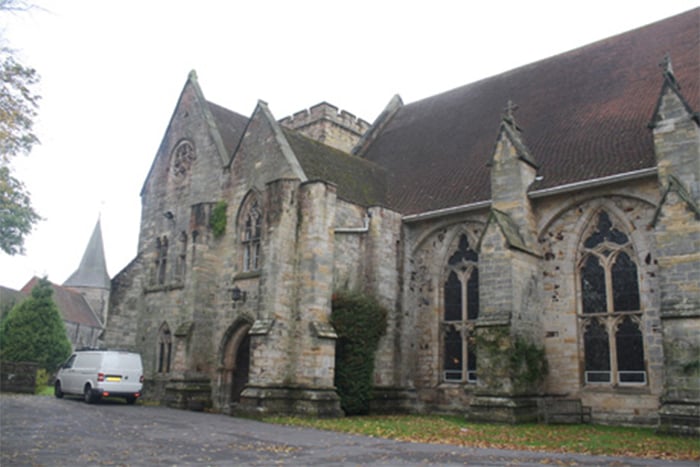 A large grey stone church building with buttresses and diamond-leaded windows