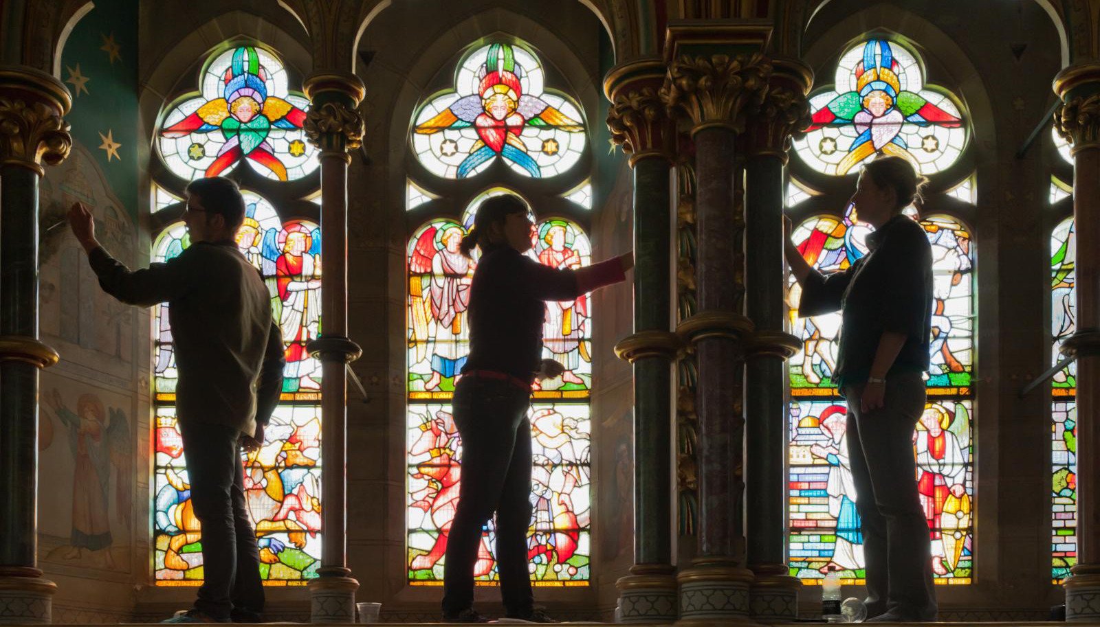 Photo of people silhouetted against stained glass windows
