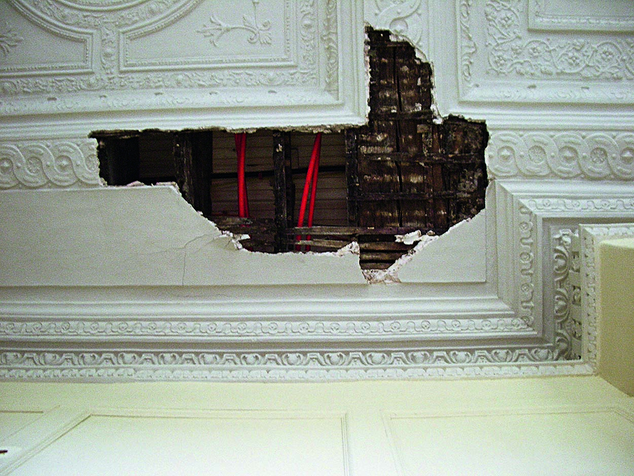 A large hole in a decorative plaster ceiling exposes pipes in the ceiling void.