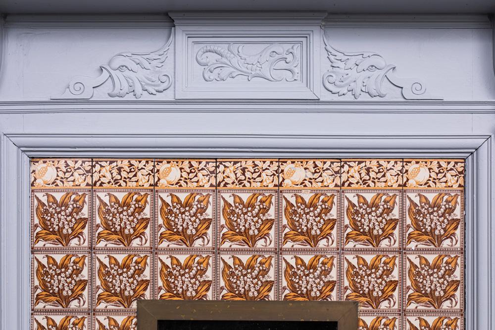 Fireplace tiles with lily of the valley design bordered at the top with pomegranate and foliage design.
