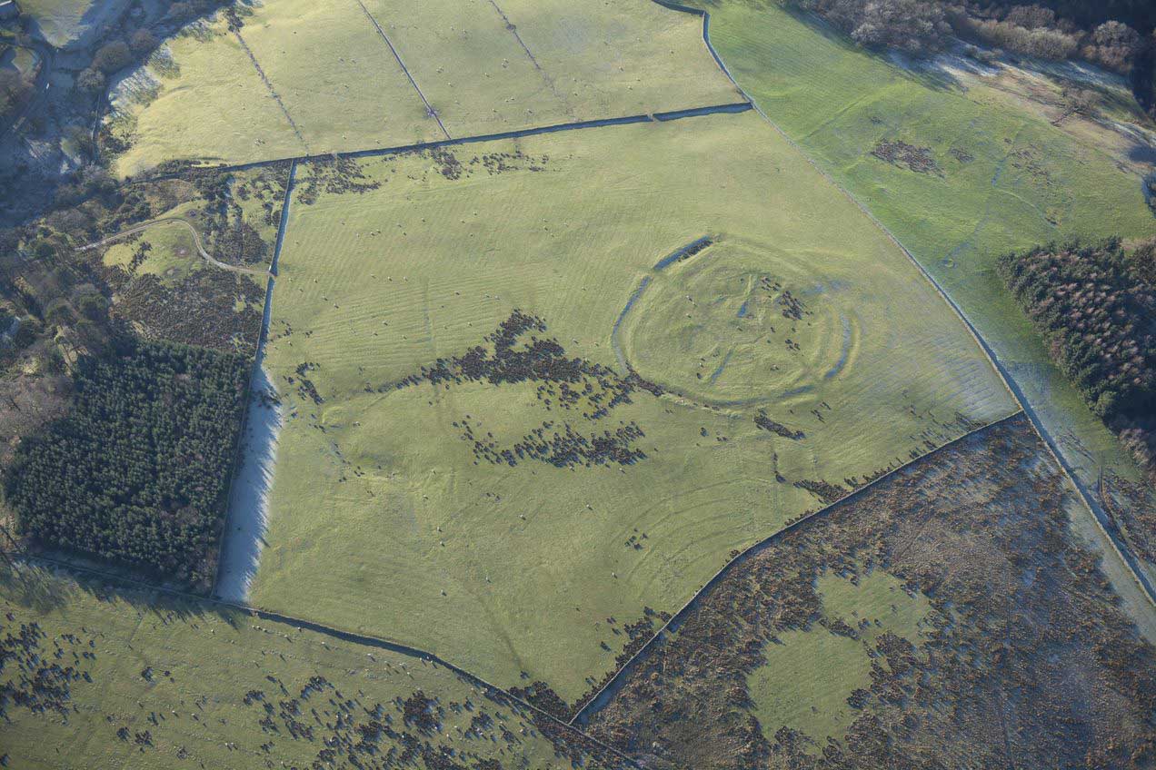 An aerial photograph of a circular enclosure on a hilltop seen as earthworks.
