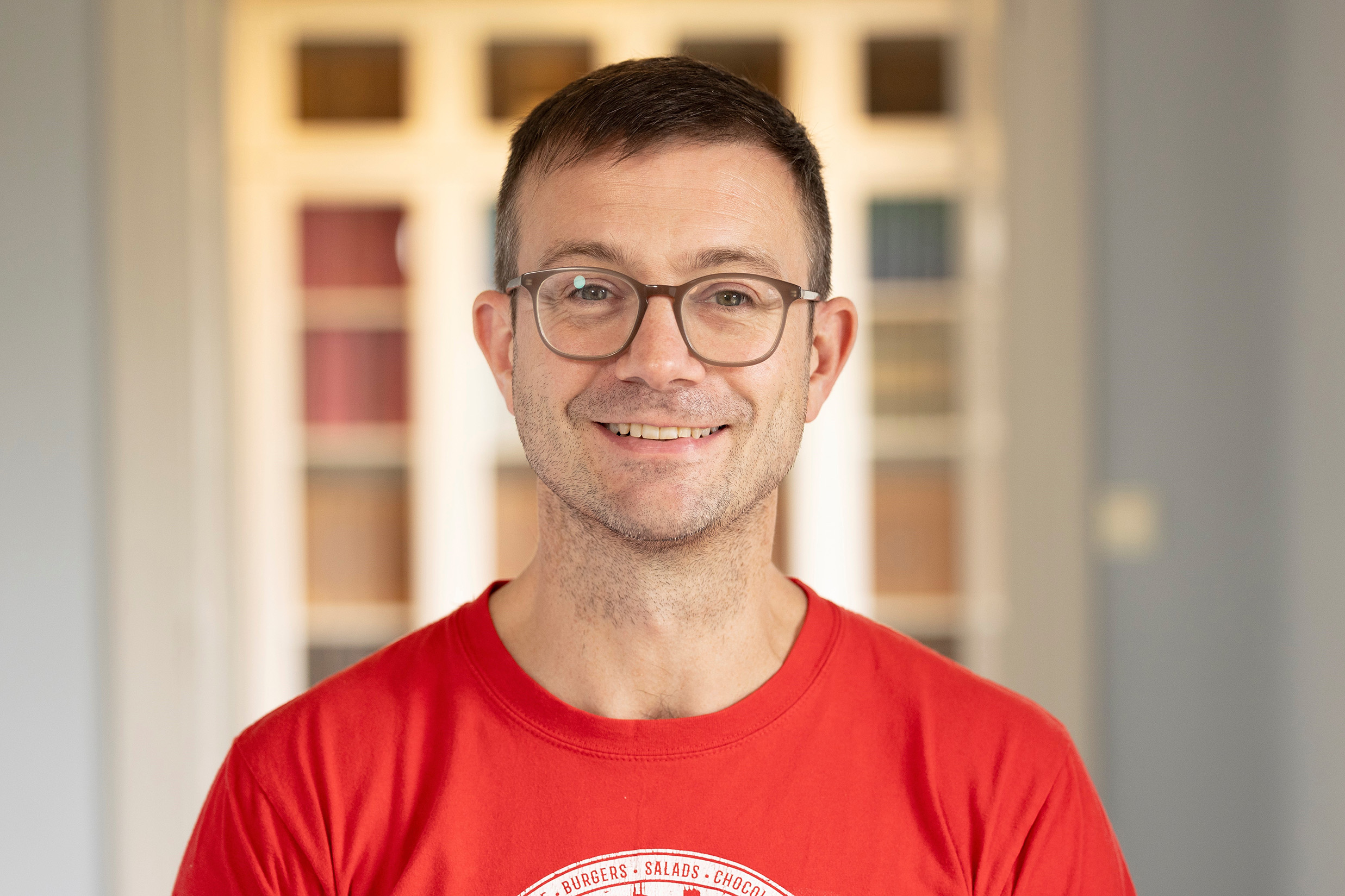 A head and shoulders portrait photograph of Jerome De Groot smiling in a red t-shirt