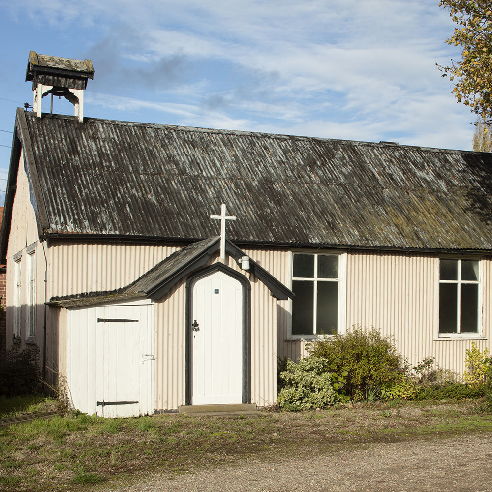 A small church made out of white corrugated walls and a black corrugated roof. 