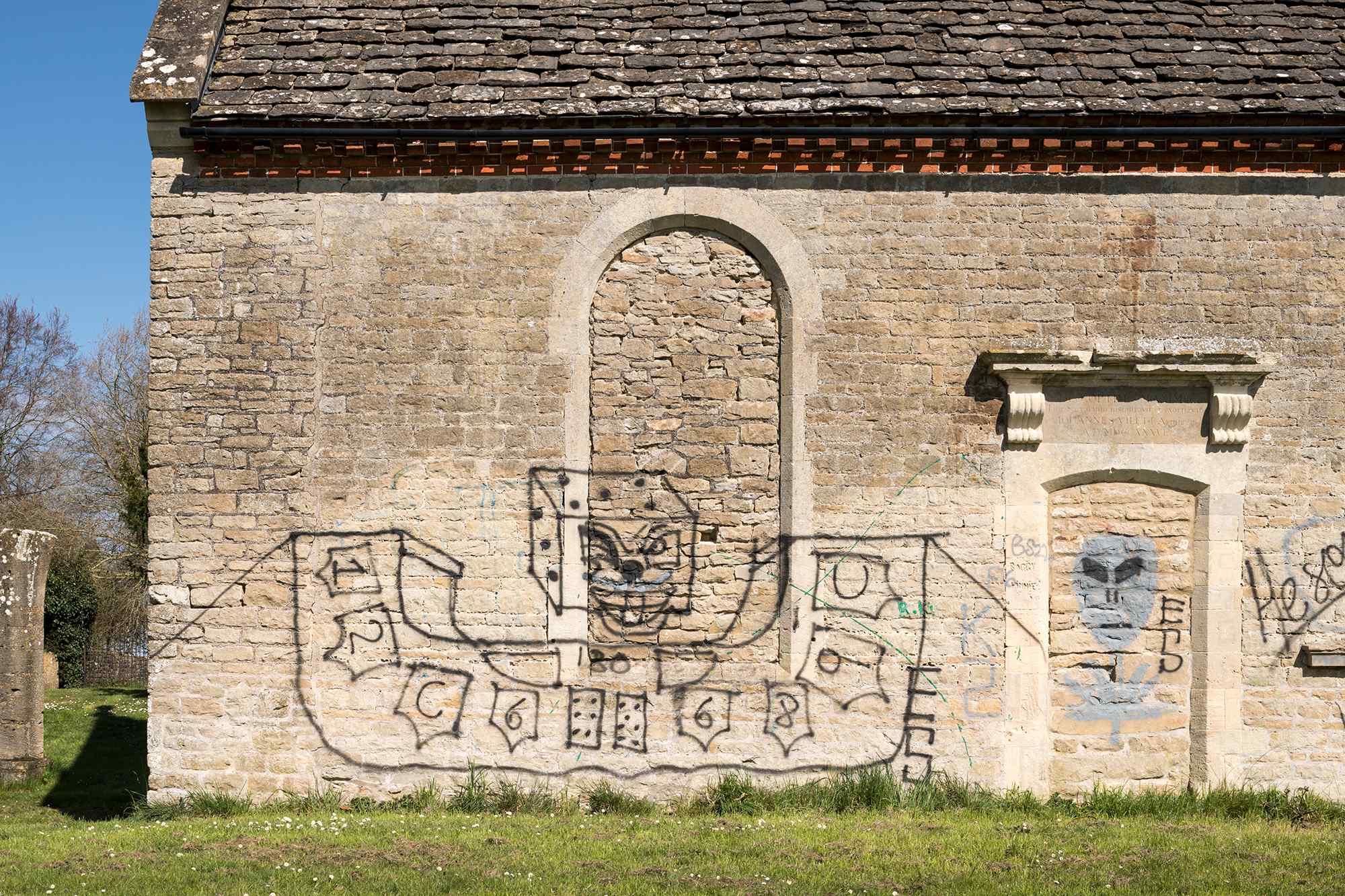 brick church building with graffiti, surrounded by grassland