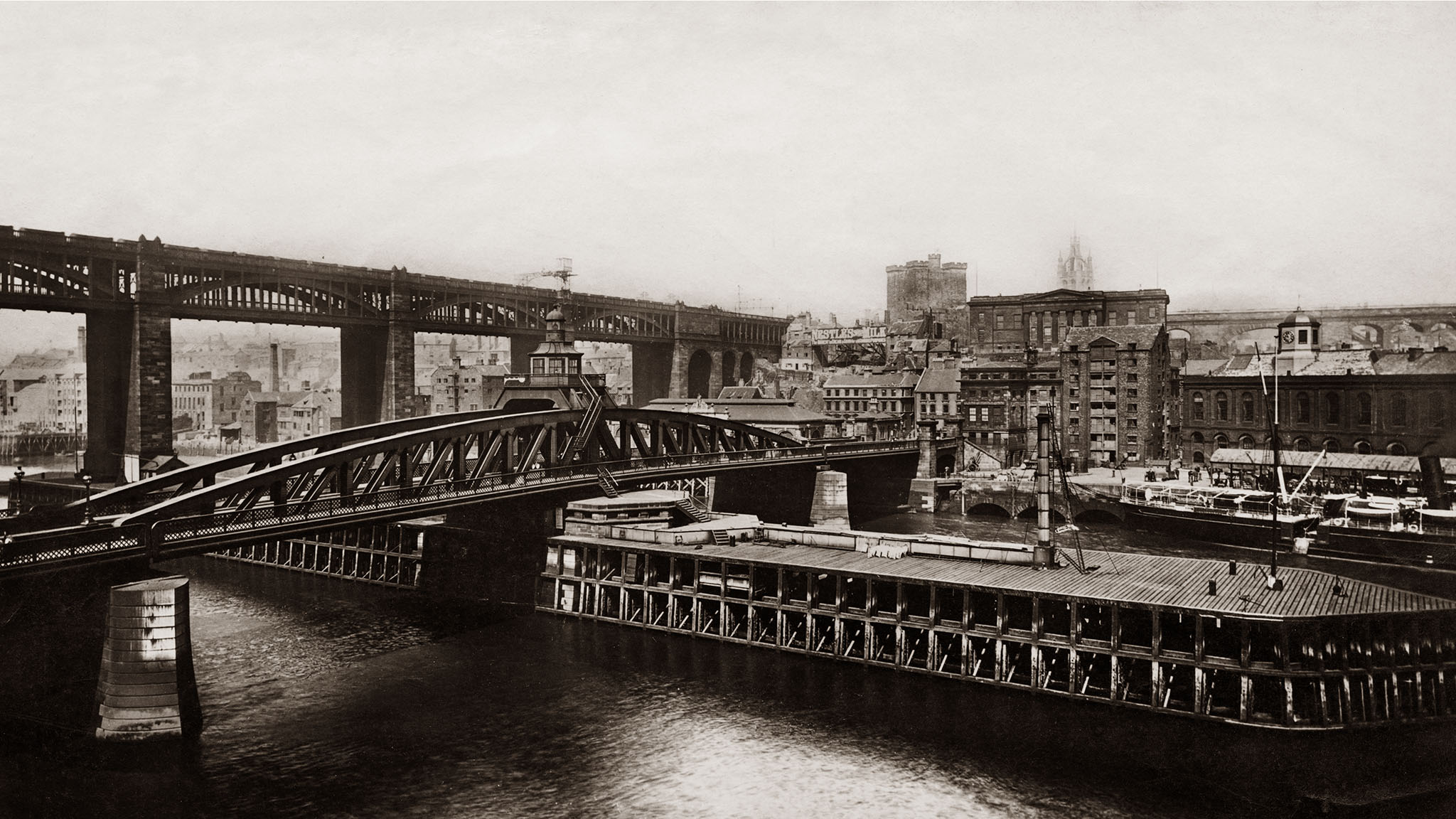 Archive sepia image showing a river with two bridges and a city beyond.