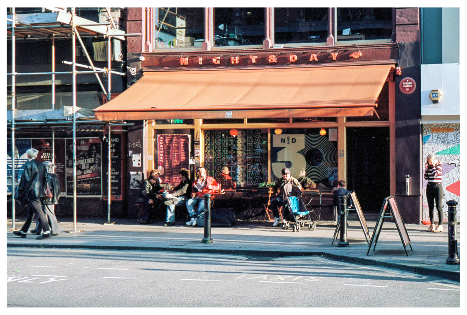 A view from across the street of the Night and Day Café, with people sitting at tables outside