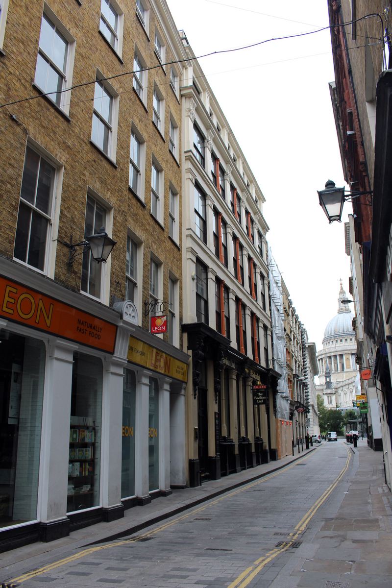 View of a narrow street lined by five-storey buildings with St Paul's Cathedral at the top