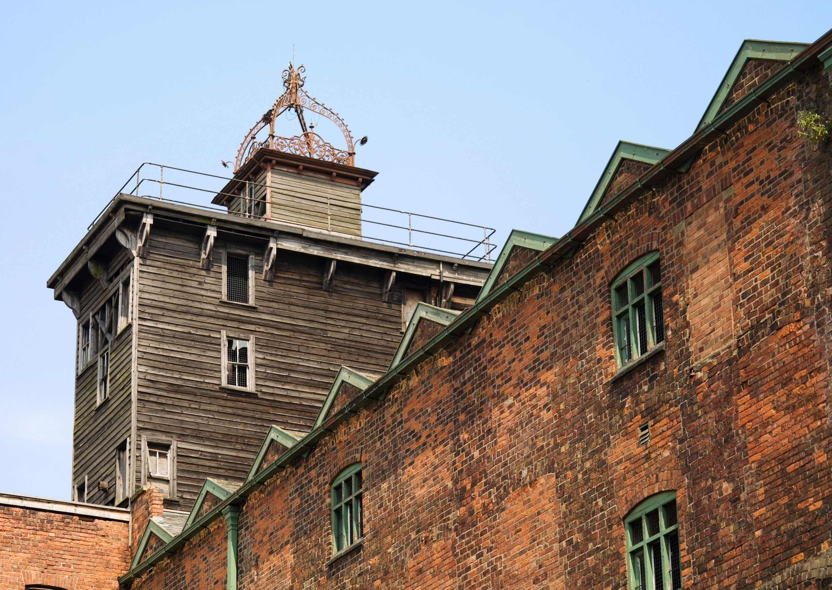 Exterior view of looking up at red brick industrial building with a wooden turret on top.