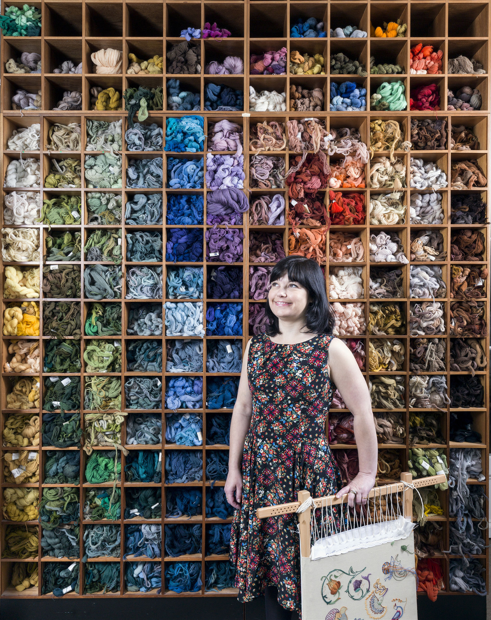 Young woman photographed in front of box shelving full of carefully organised embroidery thread.