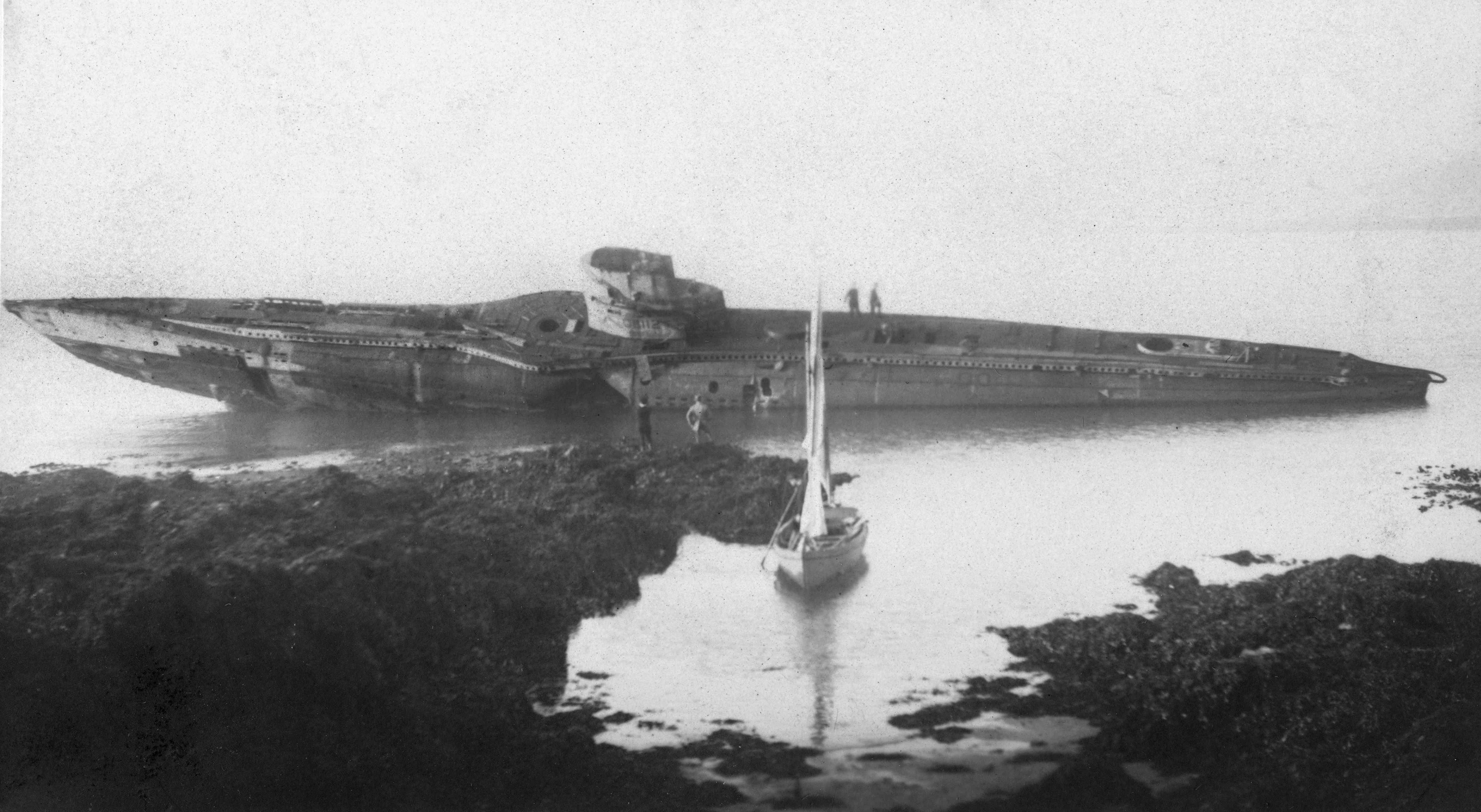 Archive image of UB-112 on the rocks with a sail boat in the foreground and visitors aboard 