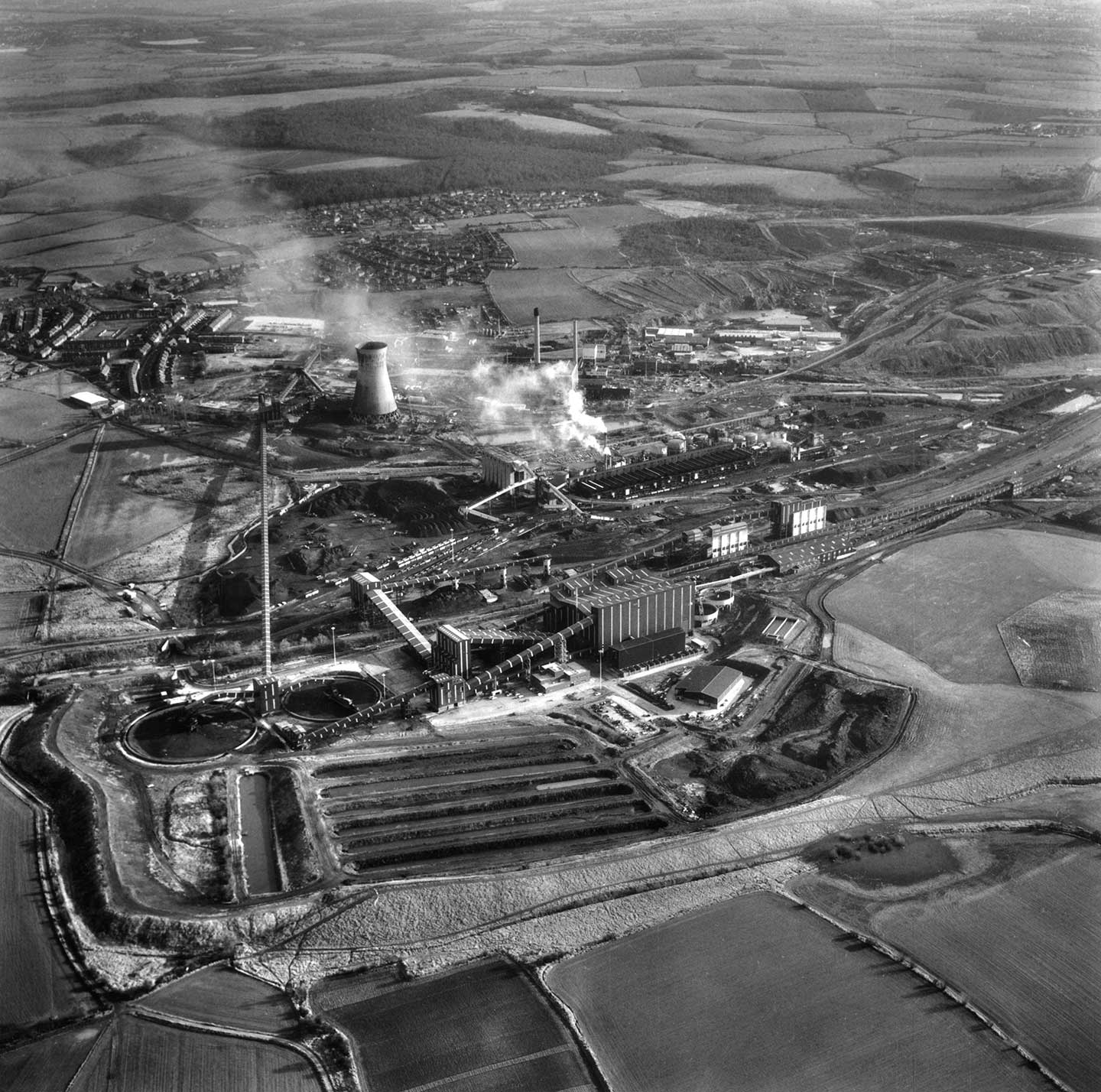 Black and white aerial photo showing an industrial complex with buildings, walkways, roads, chimneys and spoil tips
