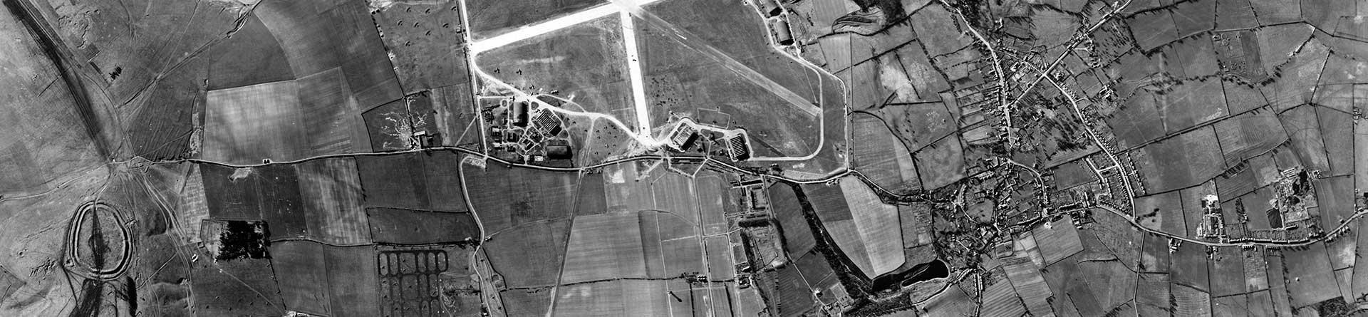 Black and white vertical aerial photograph showing an extensive landscape with fields, roads, houses and an airfield.