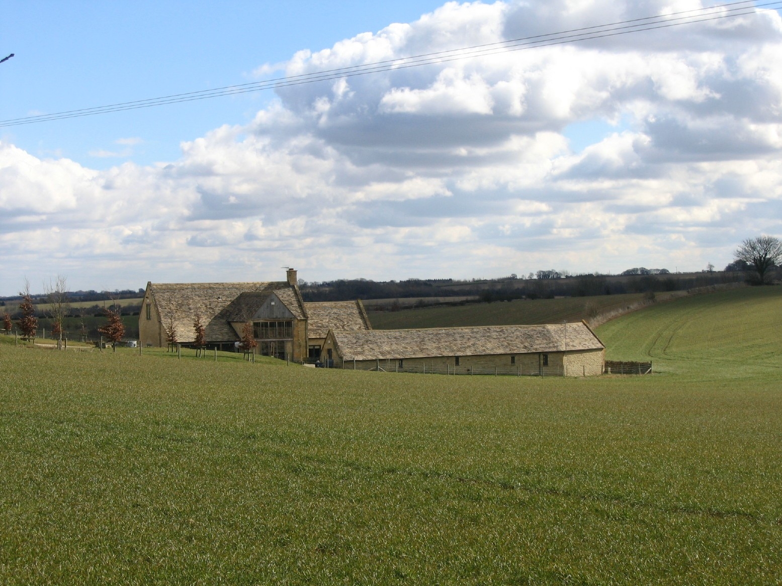 Stone farmhouse and building set in gently rolling landscape of fields of grass.