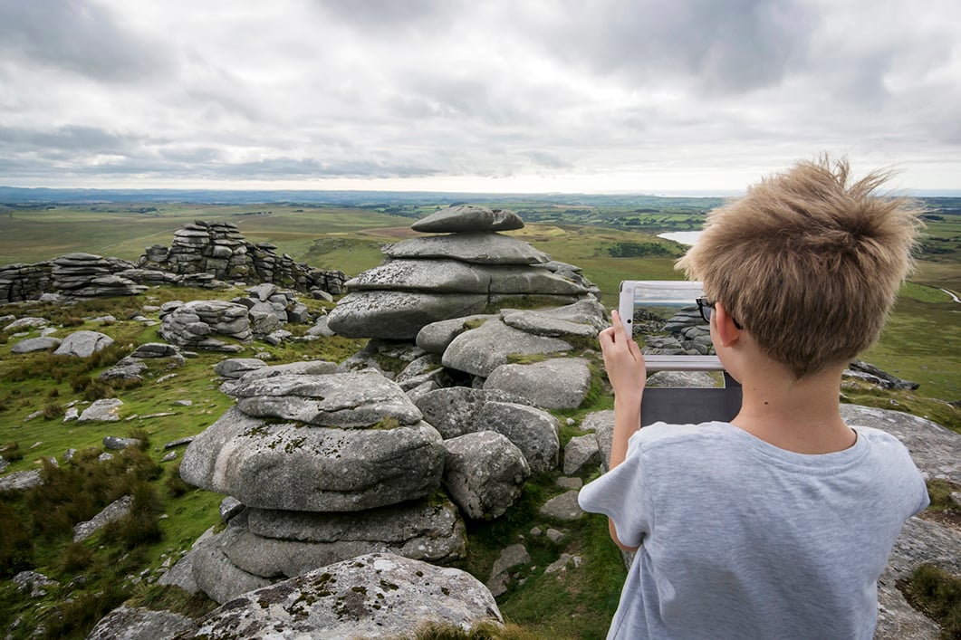 Young boy taking a photo of Bodmin Moor using a tablet.
