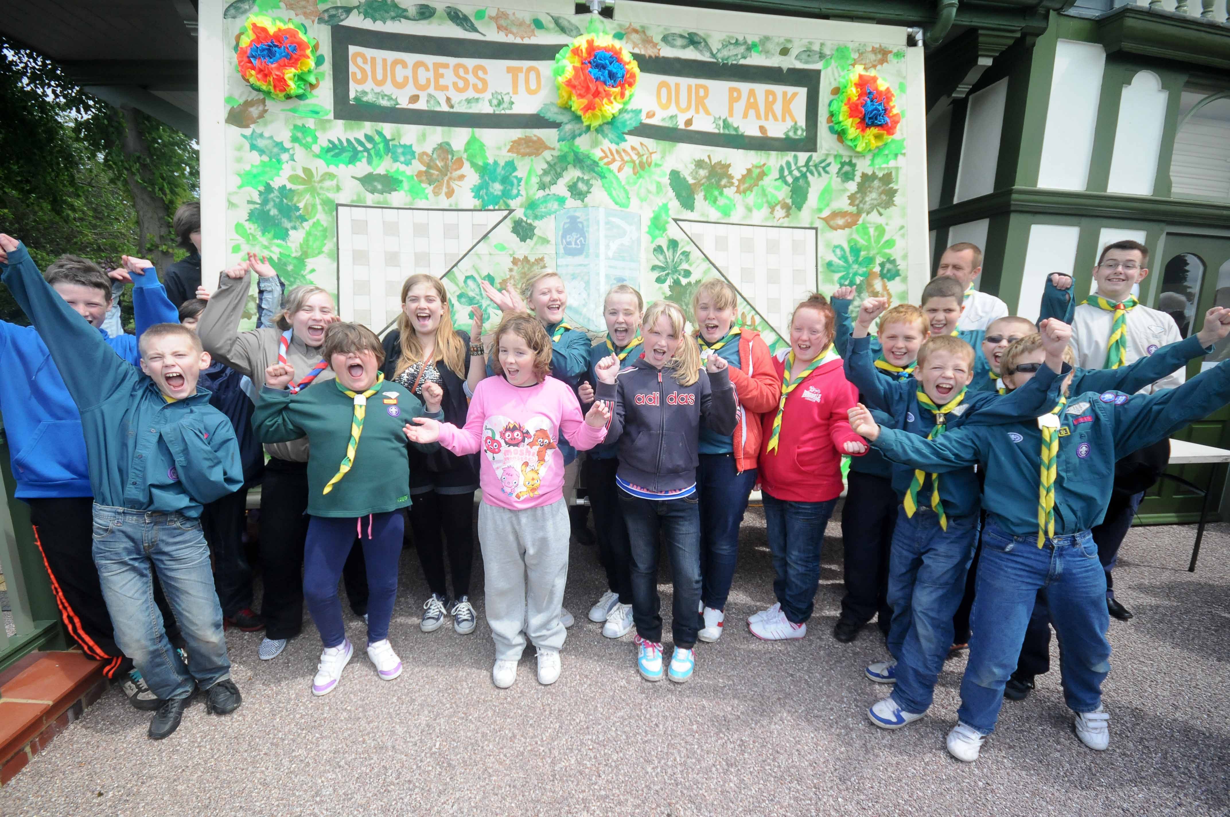 A group of young scouts celebrate in front of a poster which reads 'success to our park'