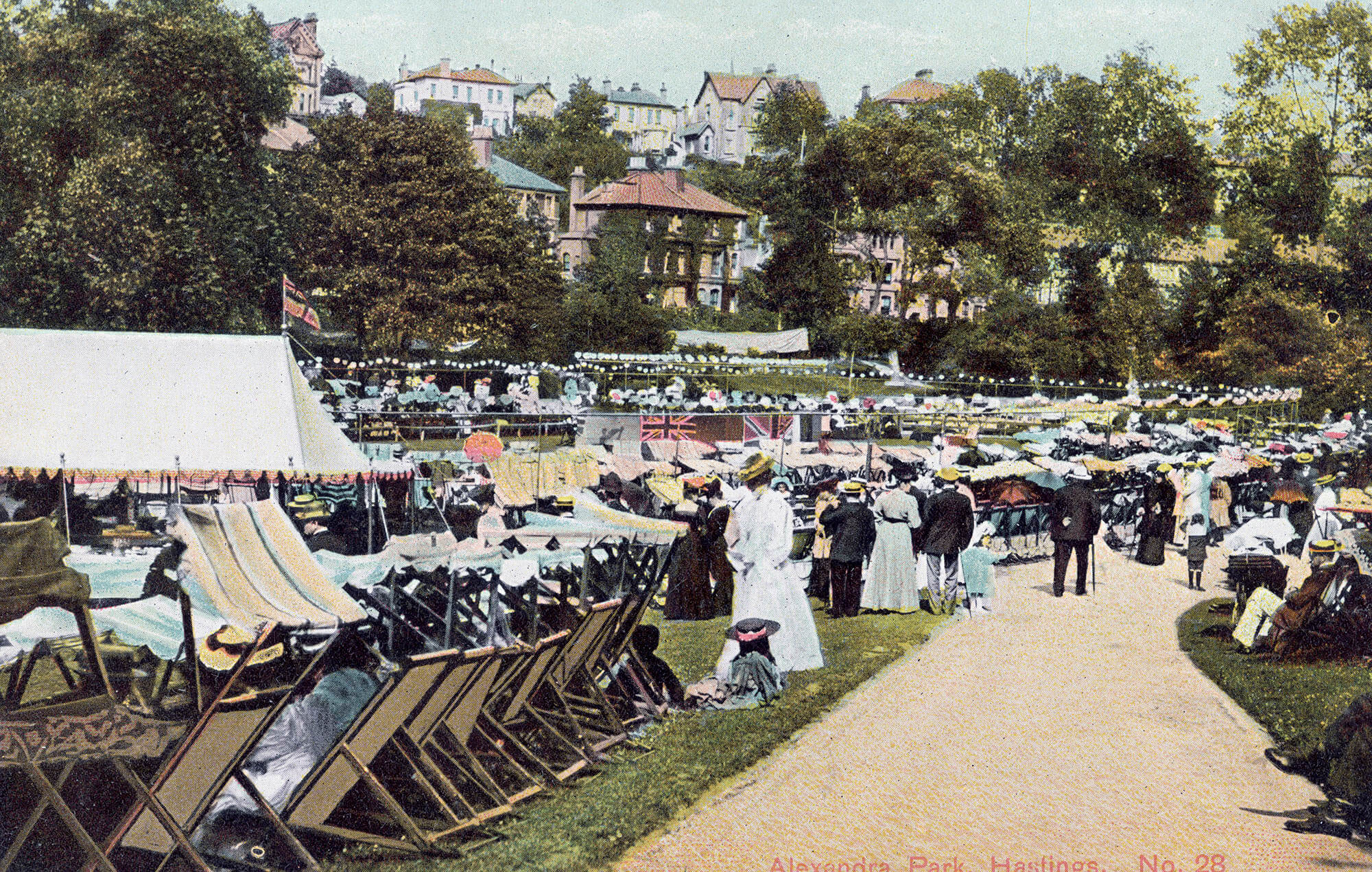Victorian postcard of visitors sat in rows of deck chairs at Alexandra Park, with houses visible in the background through the trees