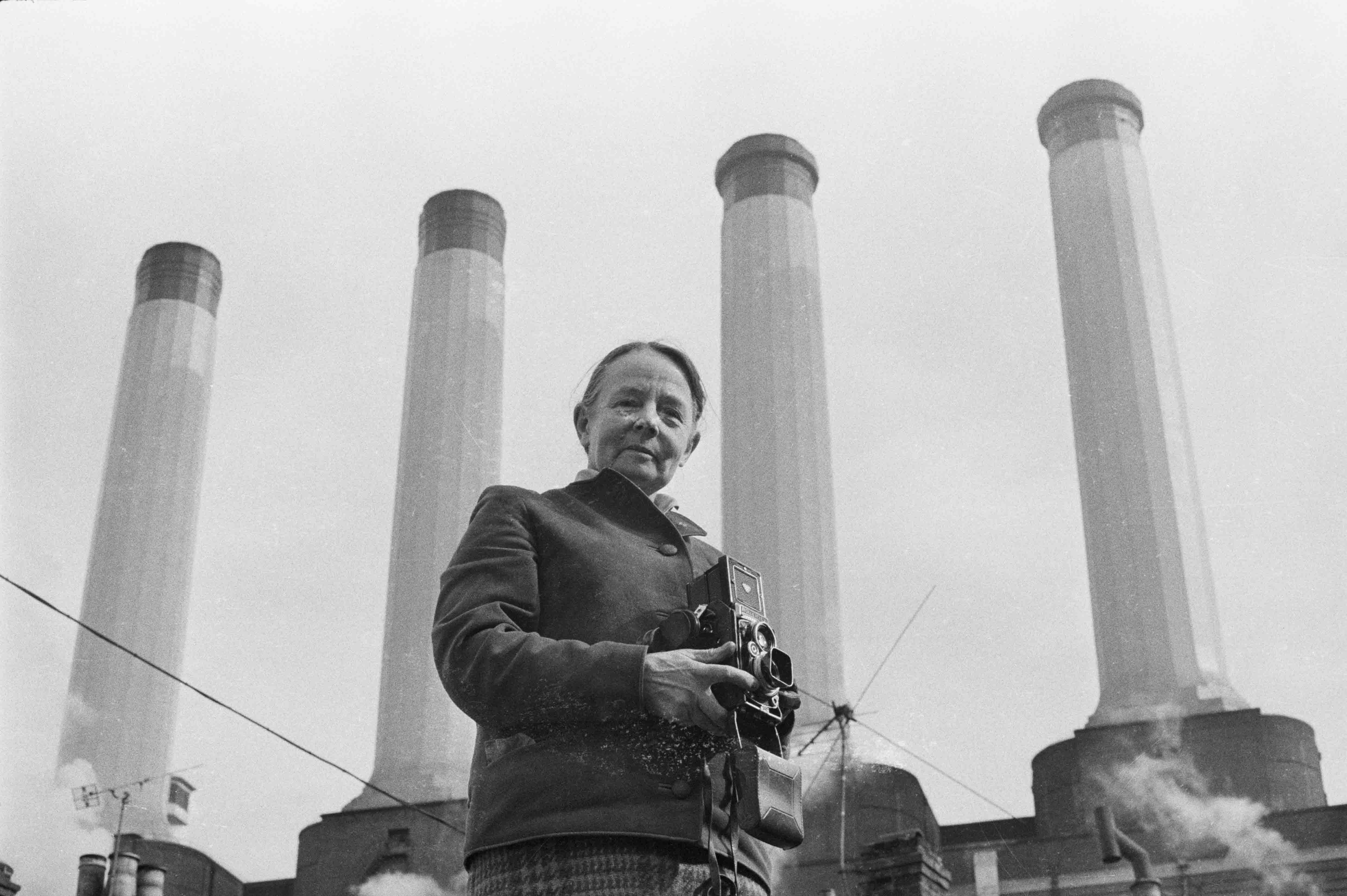 Woman holding a camera standing in front of four chimneys of a power station