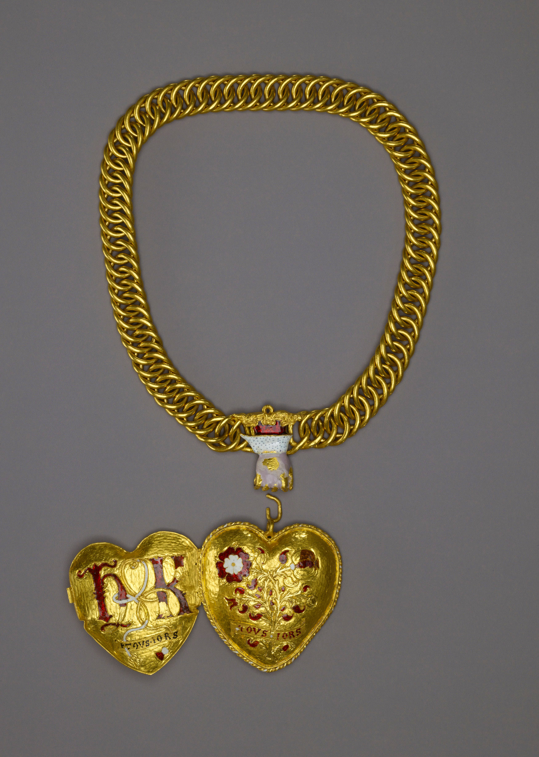 Photo of a large gold pendant on a chain. The pendant is open, showing "H K" "TOVS IORS" on one side and a floral design with "TOVS IORS" on the other.