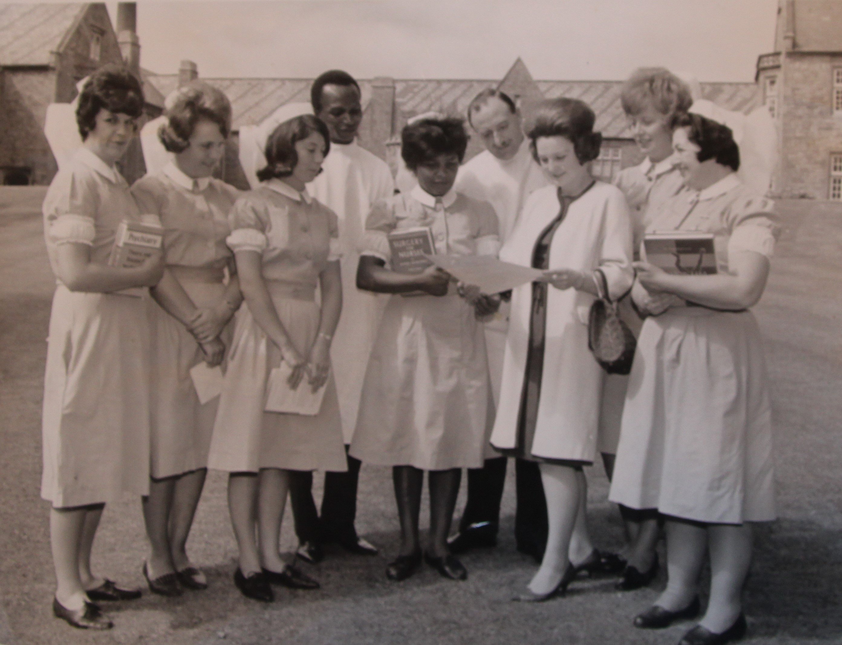 Group of male and female nurses in uniform and a woman in normal dress looking at a certificate