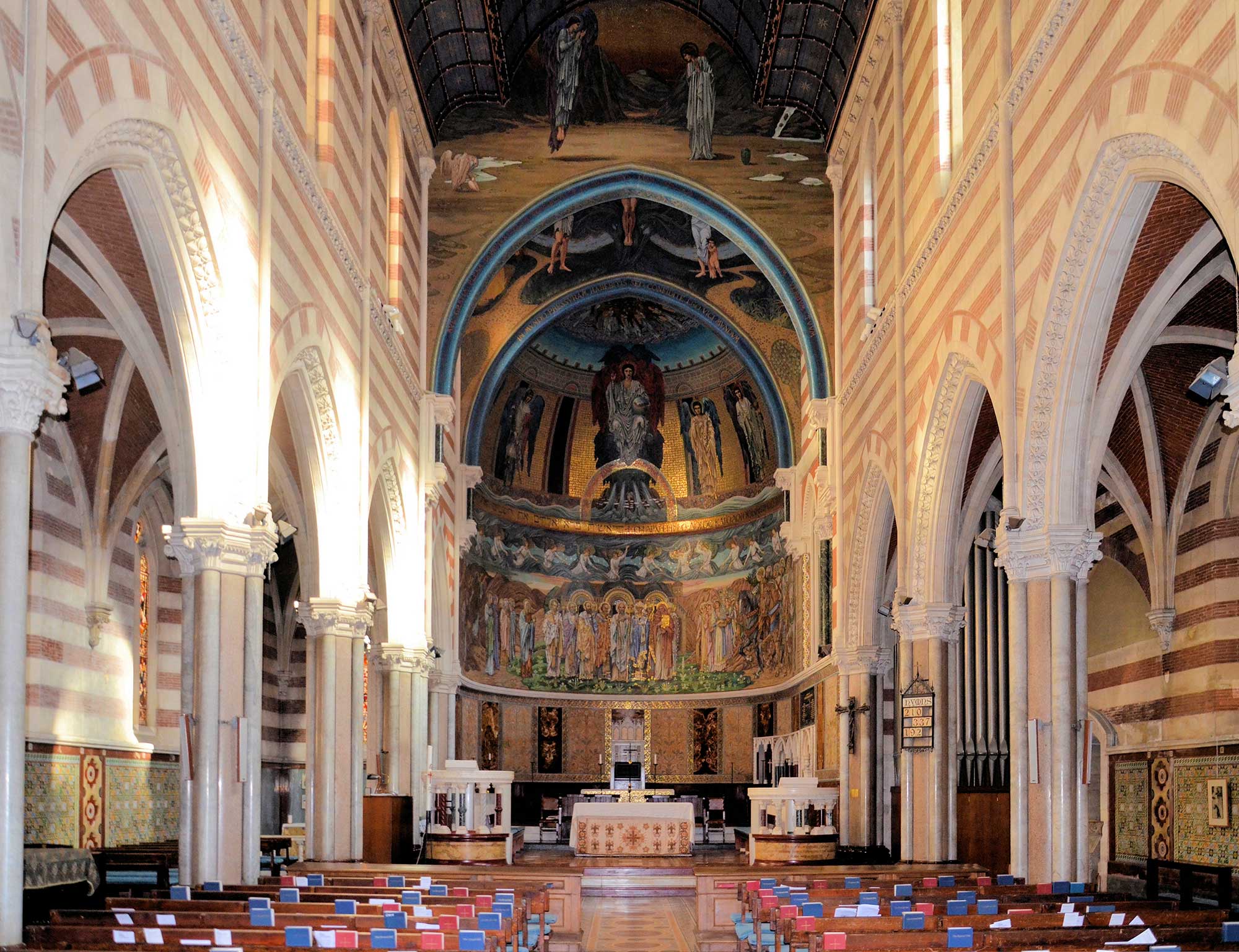 View towards the altar with elaborate paintings on the wall and ceiling. The walls are composed of alternating white stone and red brick stripes.