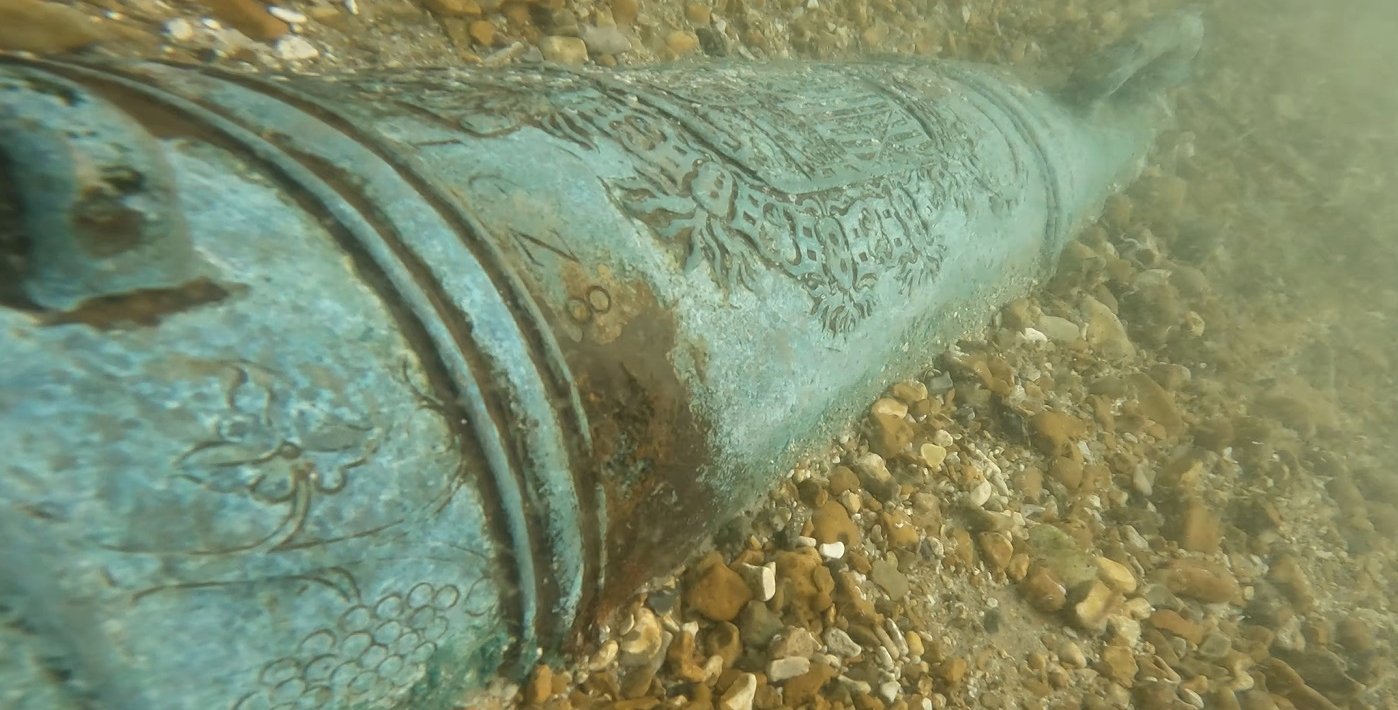 Iron cannon lying on shingle under water