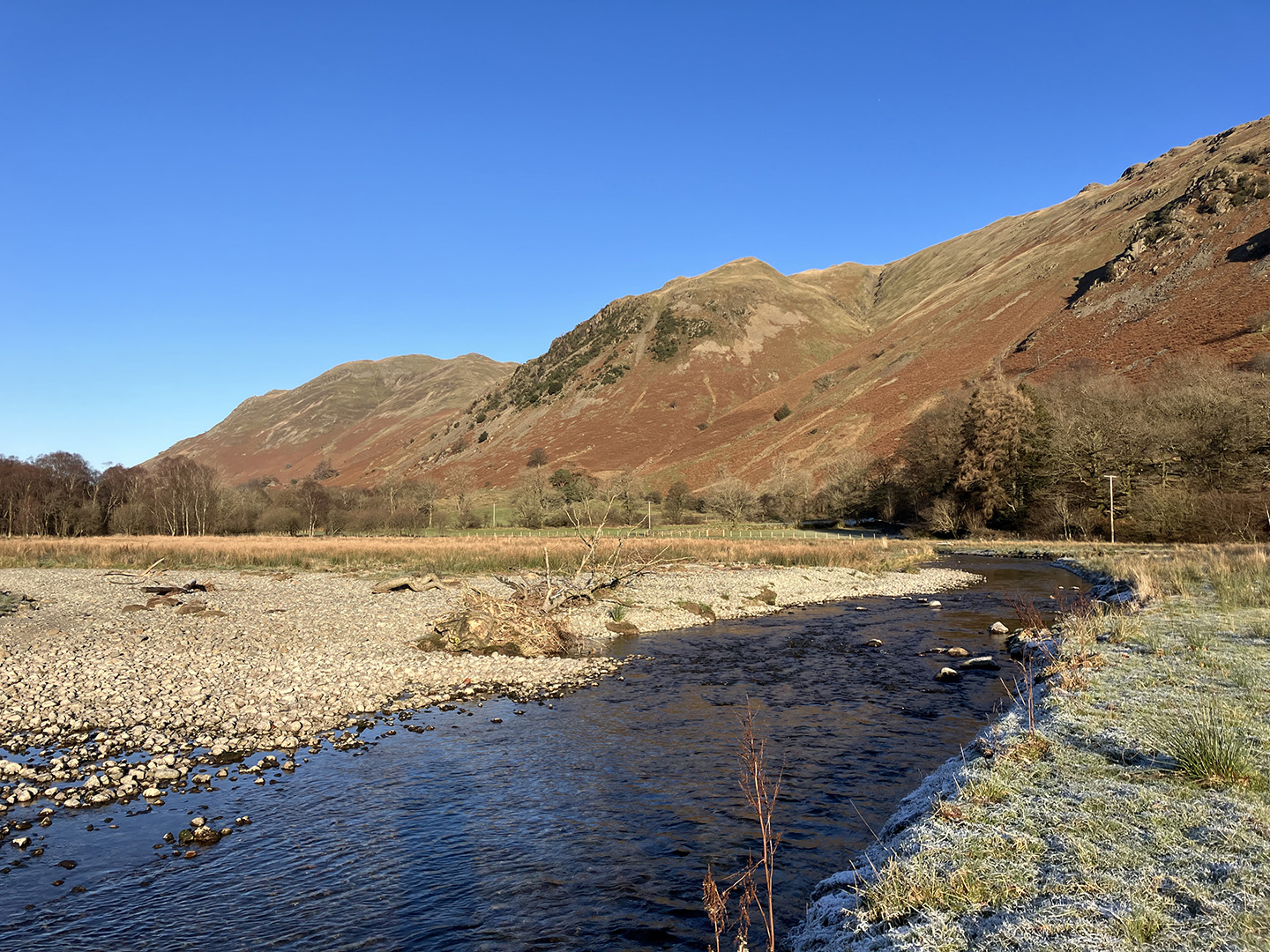  Modern colour photograph shows a section of re-wiggled river in a valley, with steep mountains rising in the distance. 