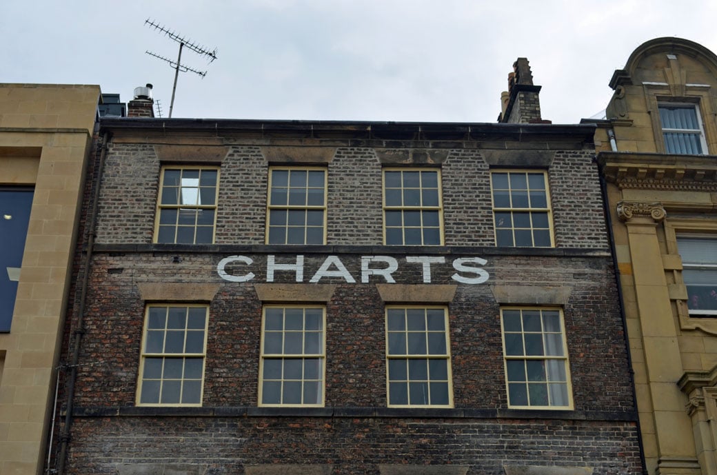Upward angle photo of the exterior of a terraced building. Painted white lettering on the brickwork reads "CHARTS"