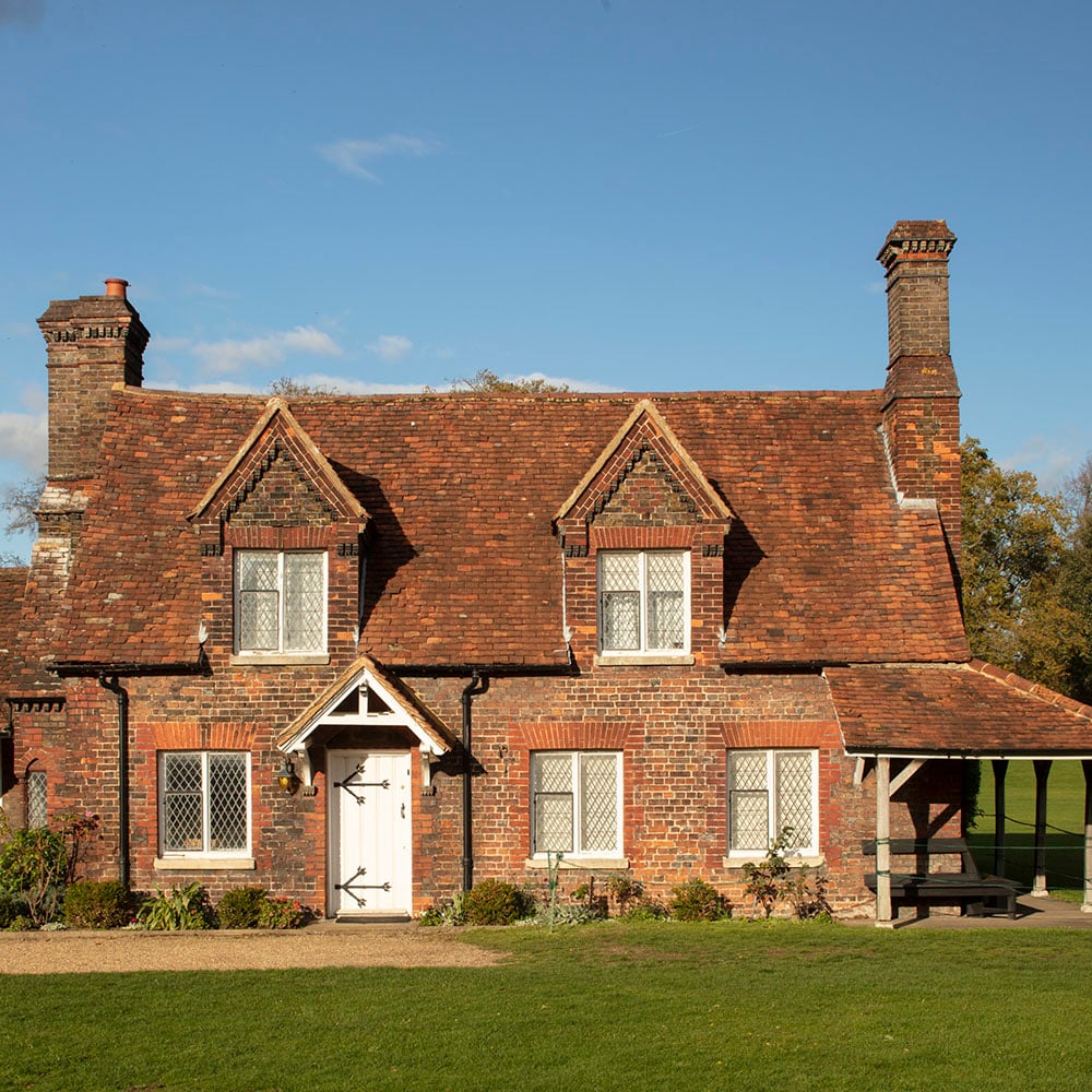 A detached brick cottage with large diamond-leaded windows and dormer windows on the upper storey.