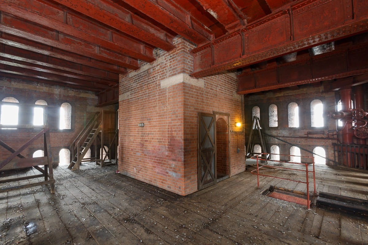 Red brick interior with dark wood floor timbers and iron girders. Many semi-circular windows can be seen.