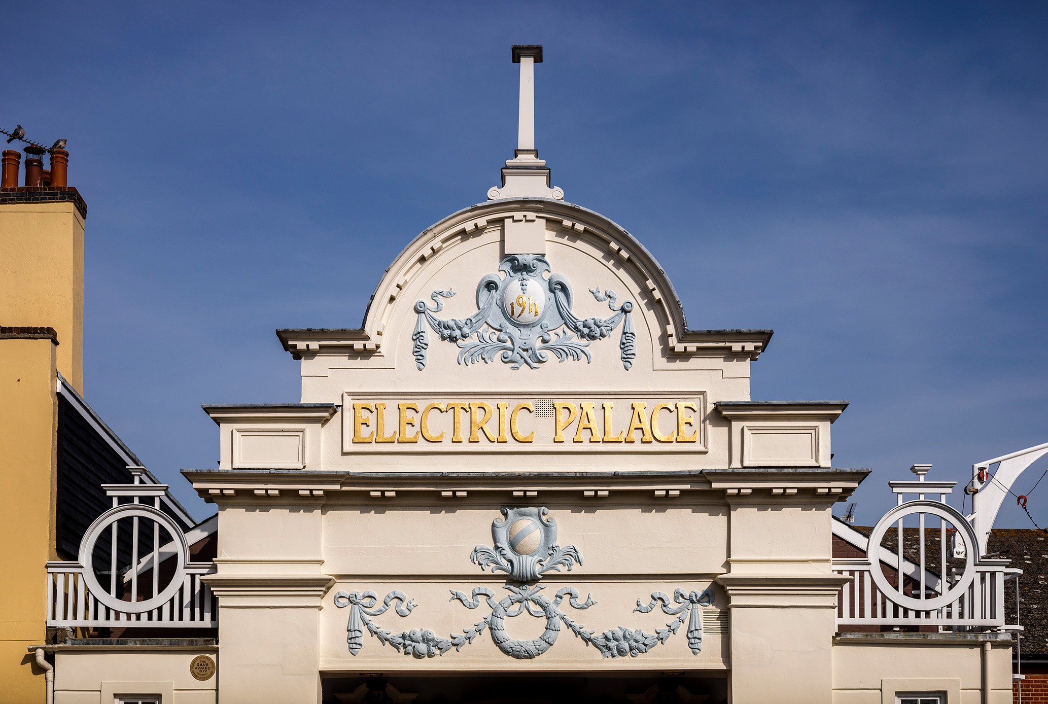The facade at the top of the exterior entrance to the Electric Palace Cinema shows scrolling decoration and the words 1911 and Electric Palace within an arched top section of the facade.