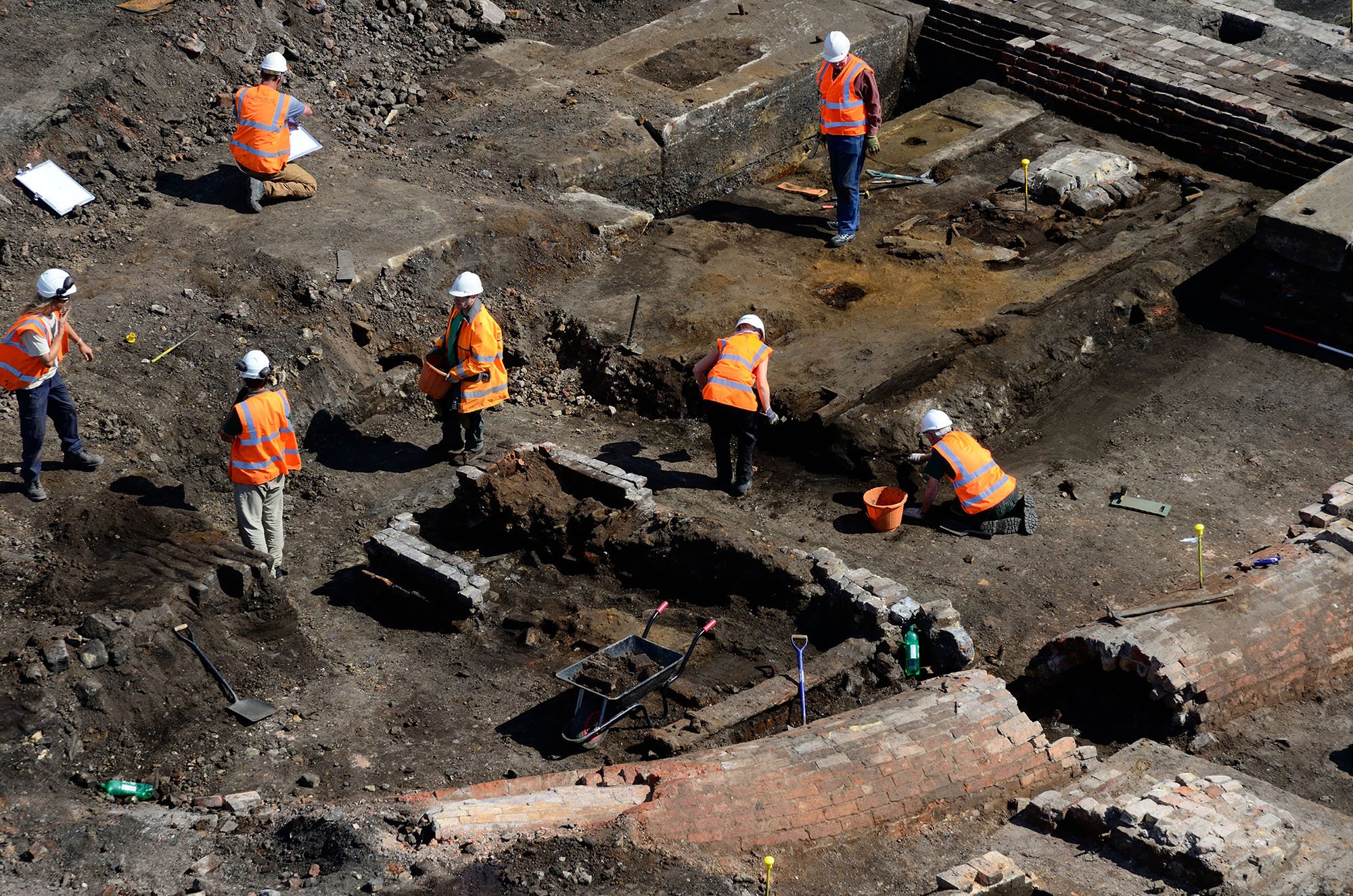 A photograph of seven people on the excavation site of a Rail Carriage and Iron Foundry site, showing building remains and footings.