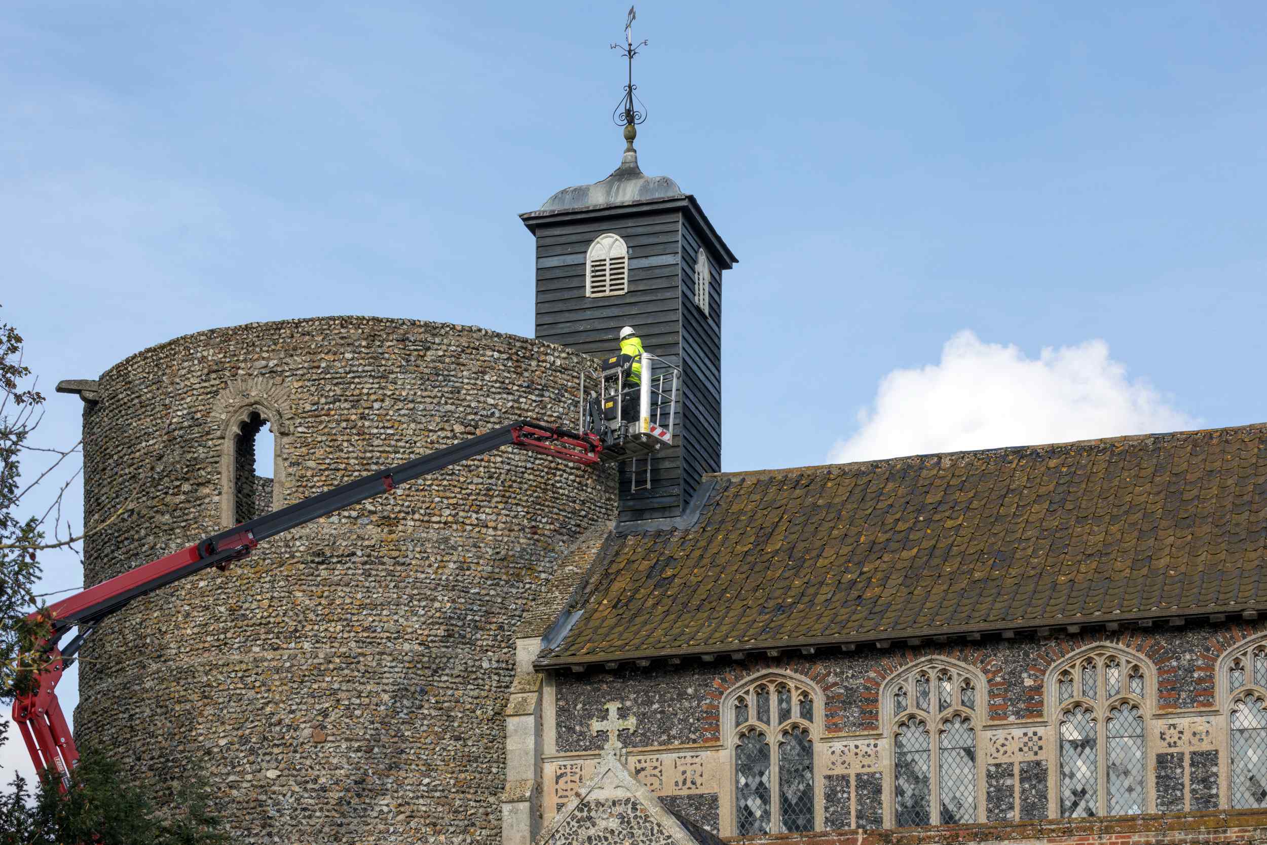 A man in high-vis jacket and hard hat works on the tower wall from a cherry picker.