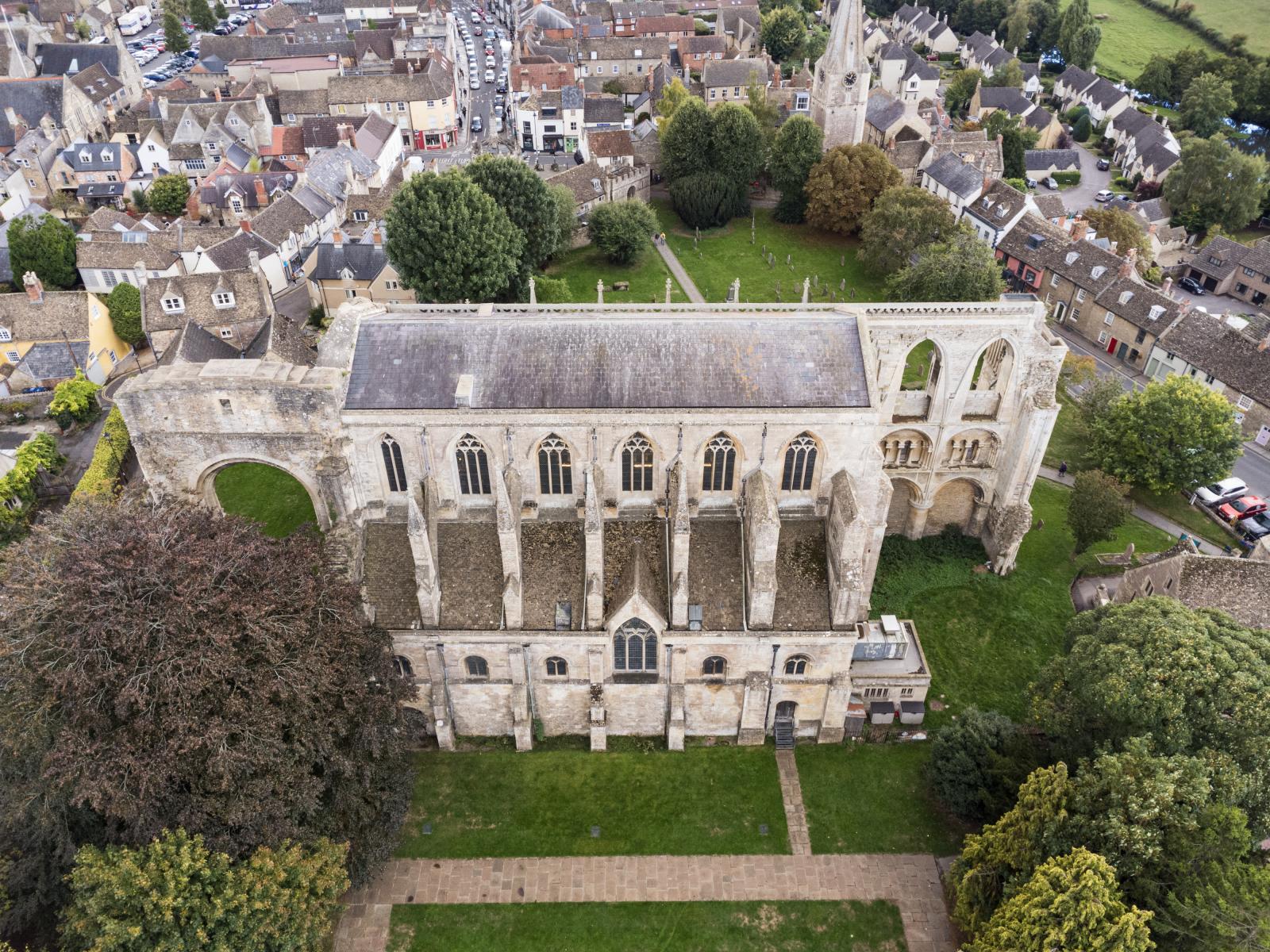 Aerial view of a large stone church with buttresses and arched windows. Ruined stonework at both ends suggests where the structure used to be much larger.