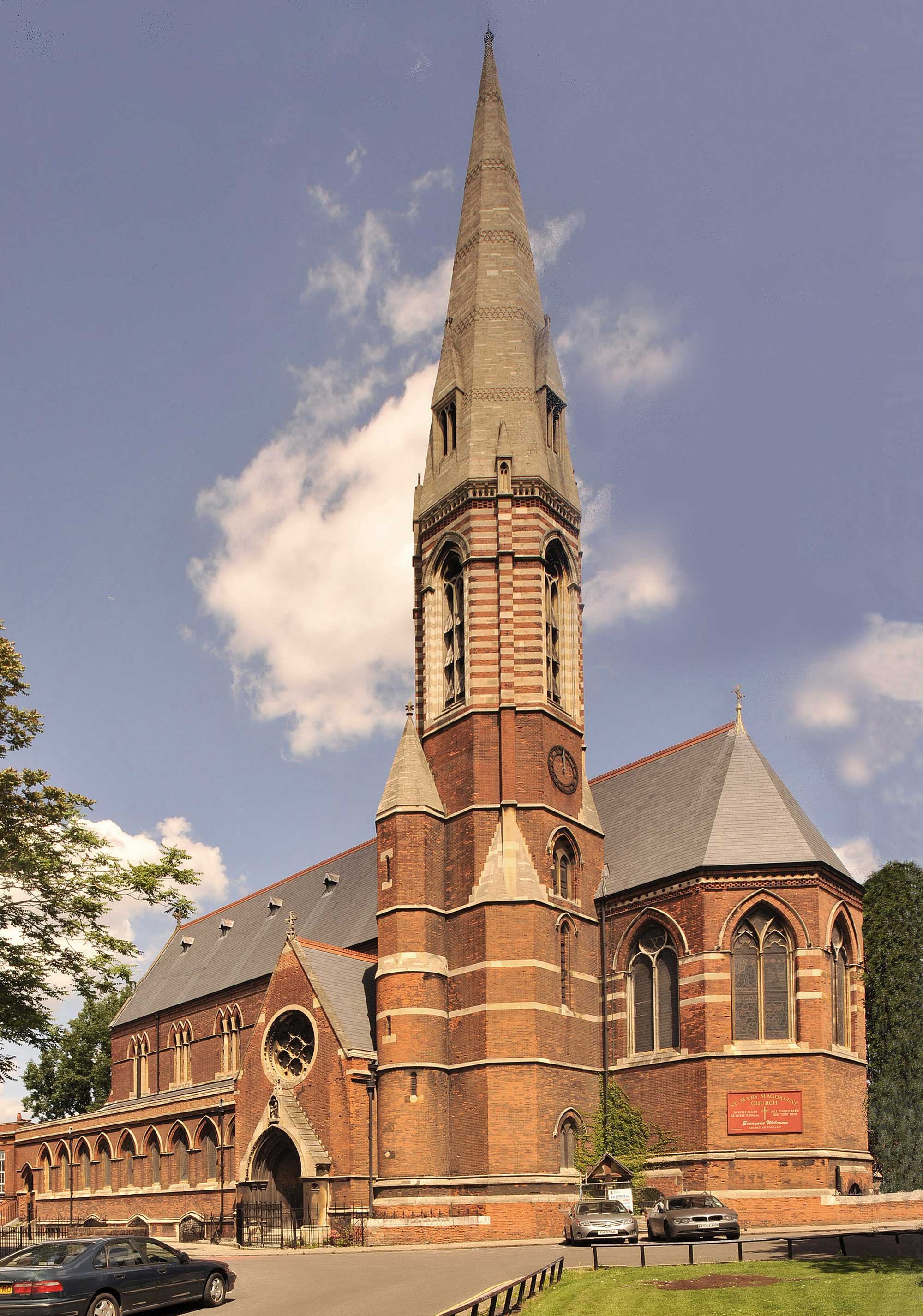 Red brick church with stone highlights and a stone spire with small windows.