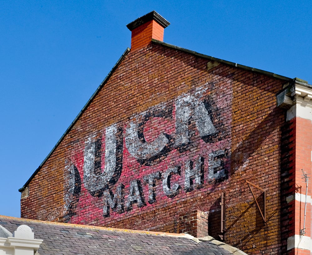 Image of the side of a brick building with a red faded advertising sign for matches.