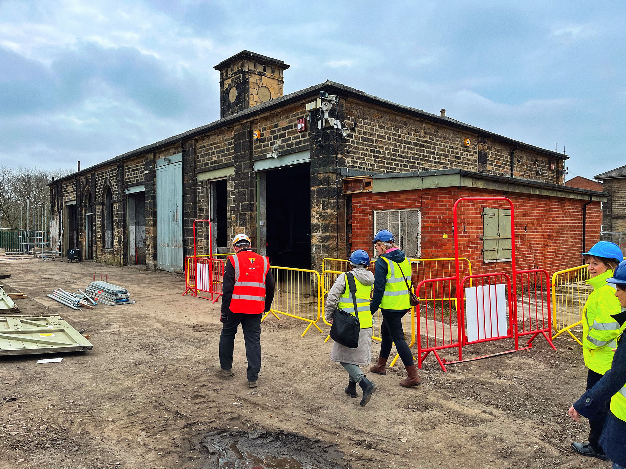 A derelict one-storey brick building with people in high vis jackets in the foreground. 